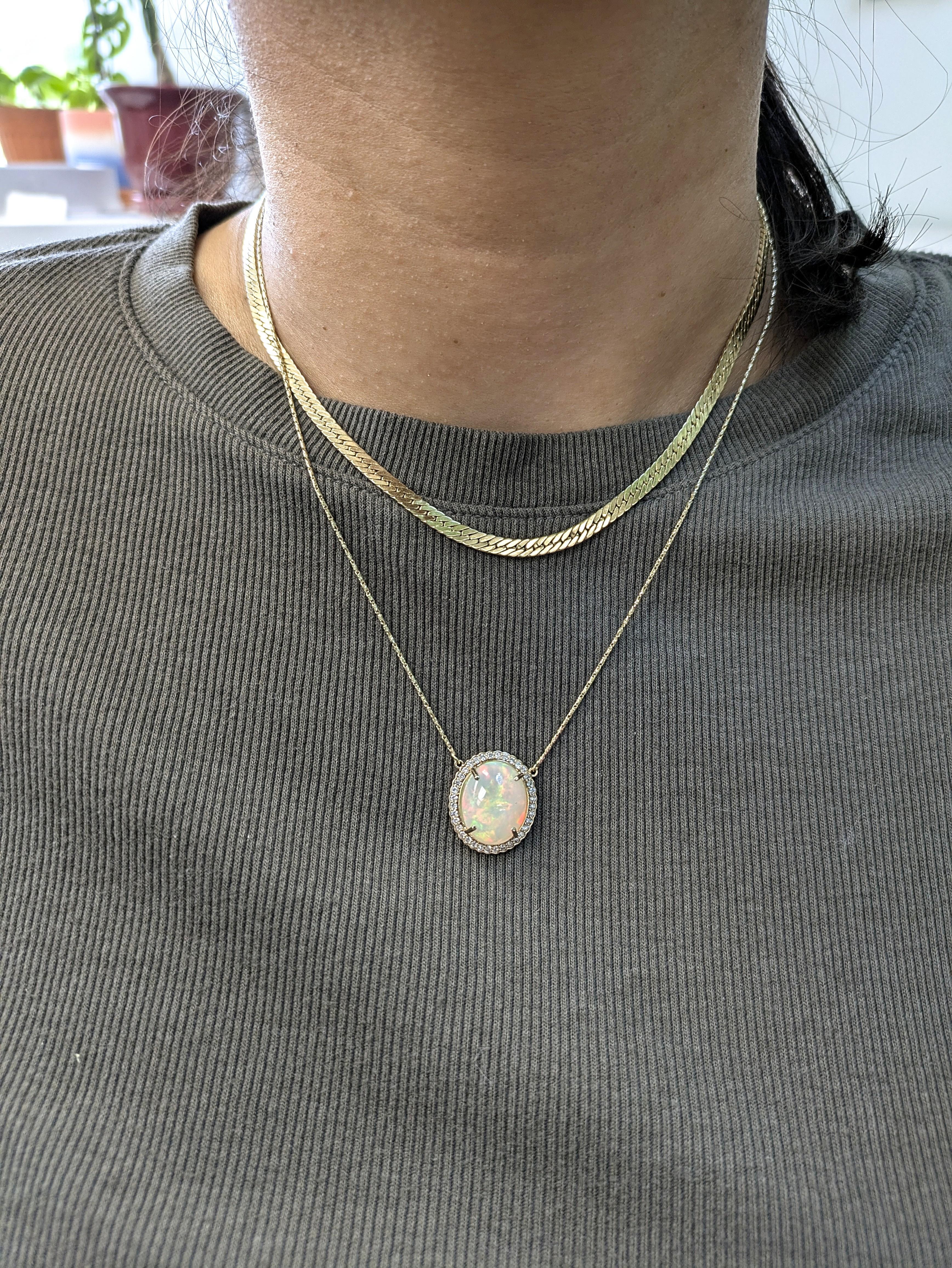 A luminous 6.36 carat Ethiopian opal takes center stage in this captivating pendant, cradled in a halo of natural, earth-mined diamonds that sparkle like stardust. Set in solid 14k yellow gold, the oval cabochon gem glows with dreamy flashes of