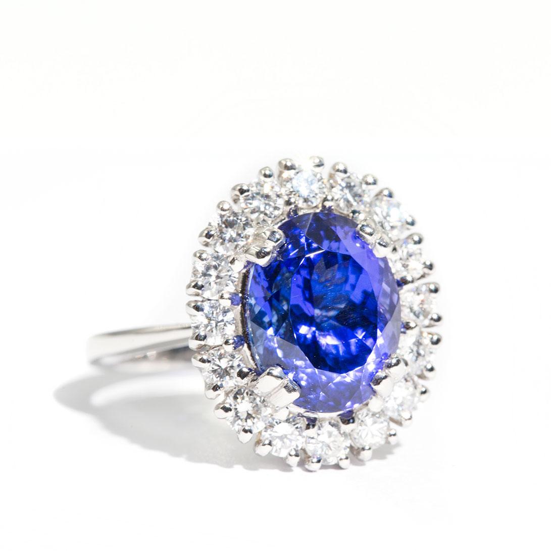 Forged in Platinum is this charming halo cluster ring featuring an enchanting oval  6.47 carat tanzanite encompassed by sparkling round brilliant cut diamonds. This uniquely designed ring bestows diamonds carefully set in an intricate gallery. The