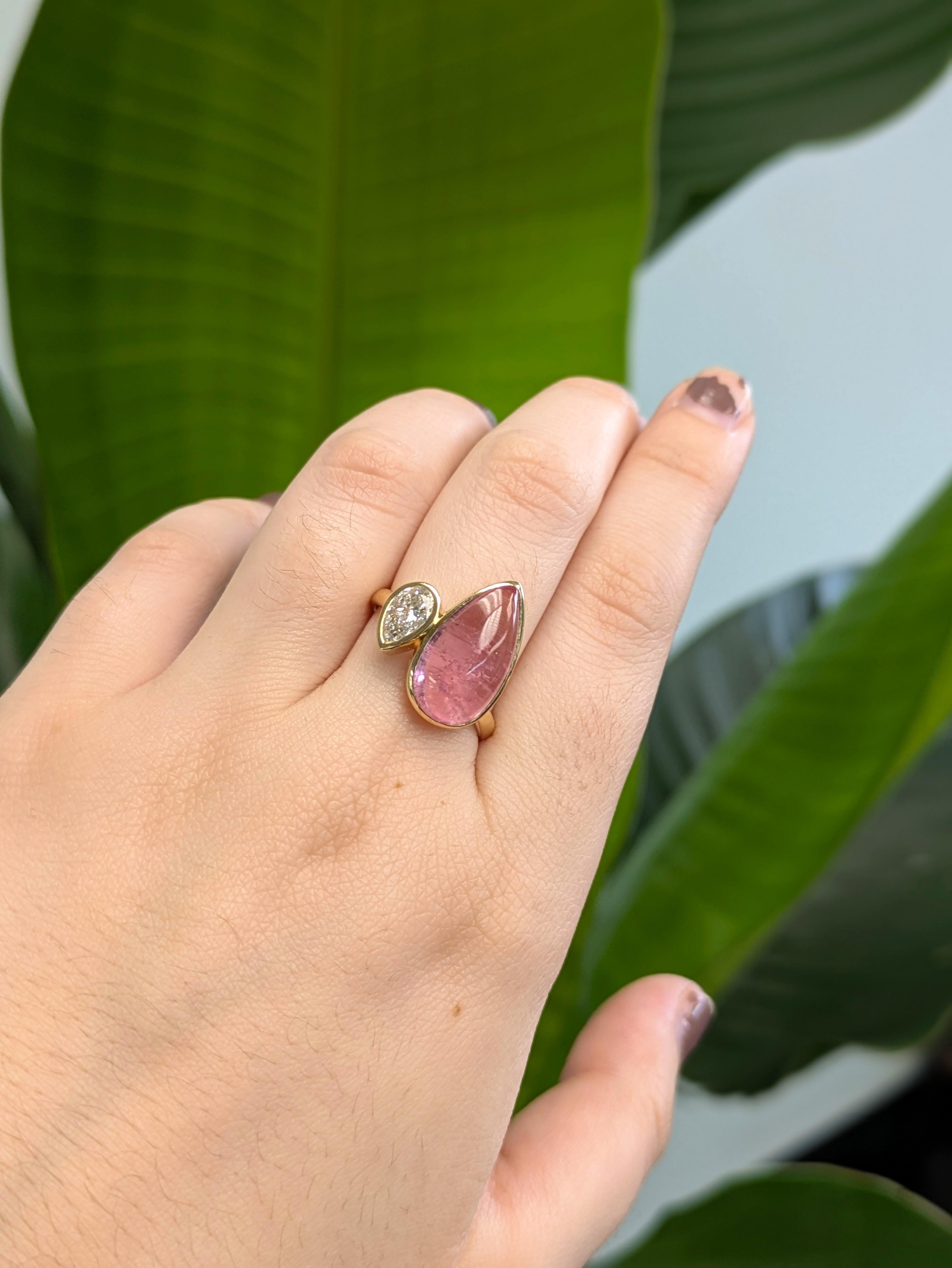 Zwei Steine, eine starke Aussage. Dieser einzigartige Ring präsentiert einen birnenförmigen rosa Turmalin-Cabochon von 6,42 Karat und einen strahlenden Labordiamanten in einer eleganten Lünettenfassung, umhüllt von schlichtem 14-karätigem Gelbgold.