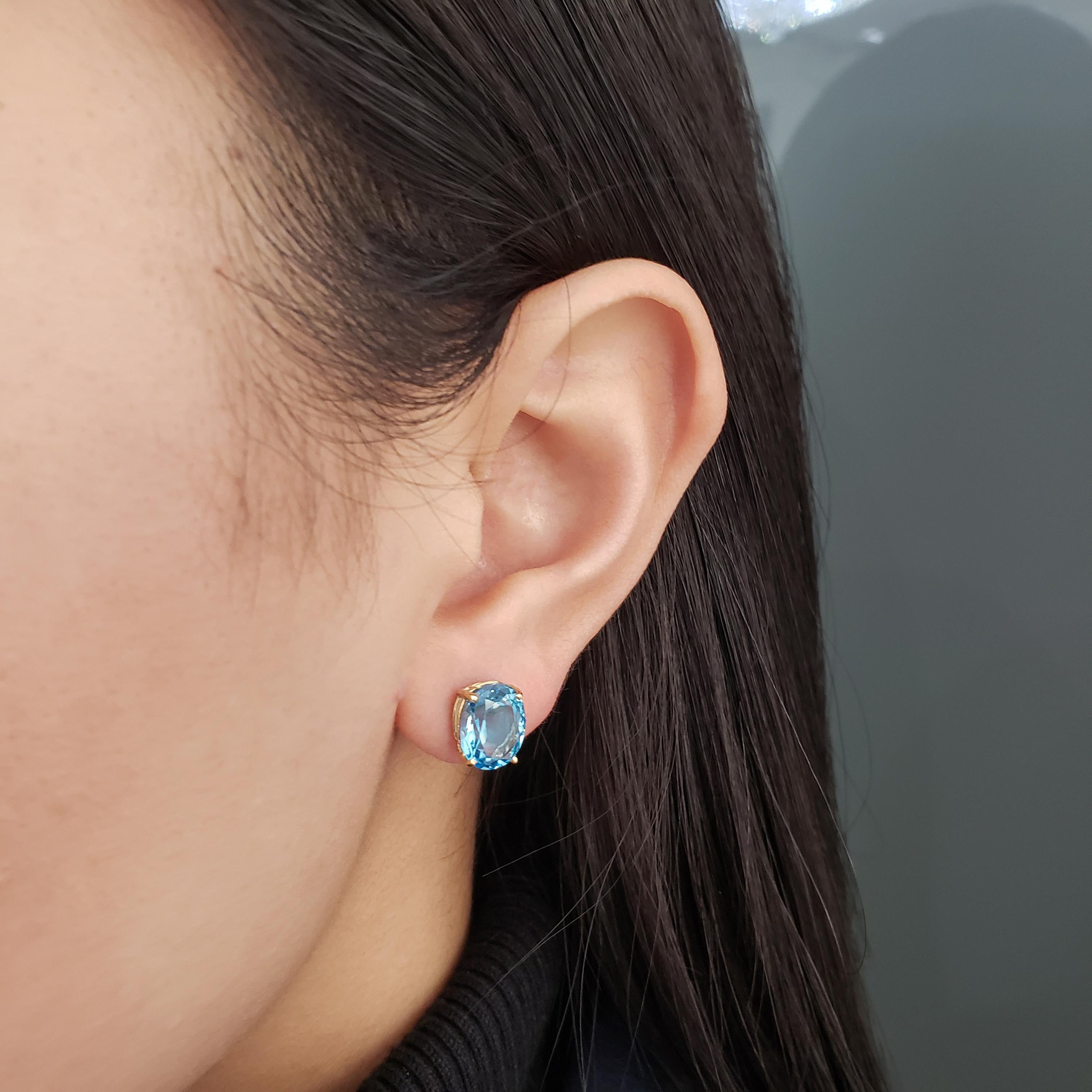 Basic and vibrant stud earrings featuring two oval cut blue topaz, set in a four prong basket made in 14k yellow gold. Topaz weighs 6.50 carats total. 