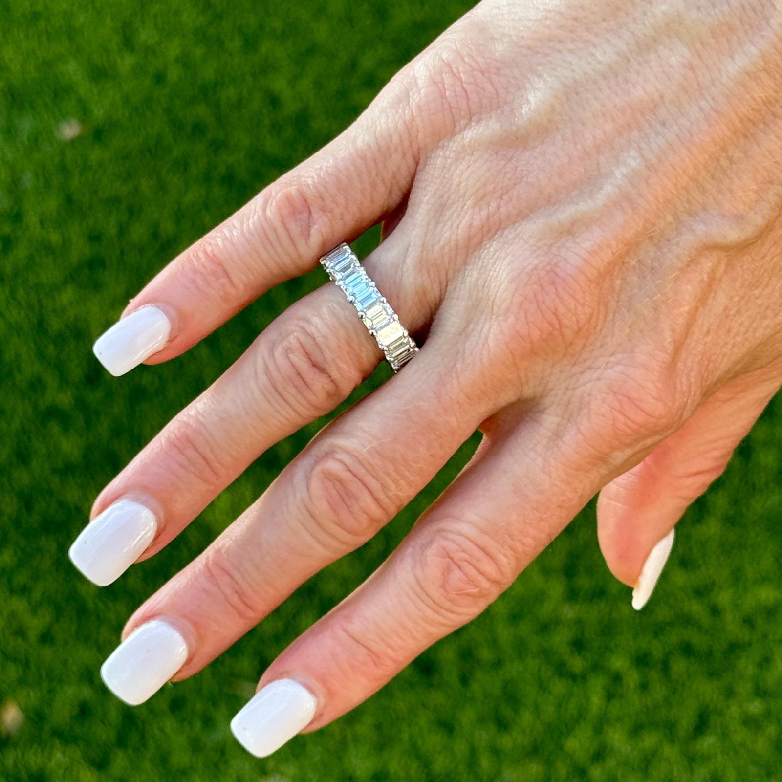 This 18 karat white gold eternity band features an elegant 'U' style setting, showcasing 22 stunning emerald-cut diamonds, totaling 6.52 carats. Graded F-G for color and VS for clarity, the diamonds offer exceptional brilliance and clarity. With a