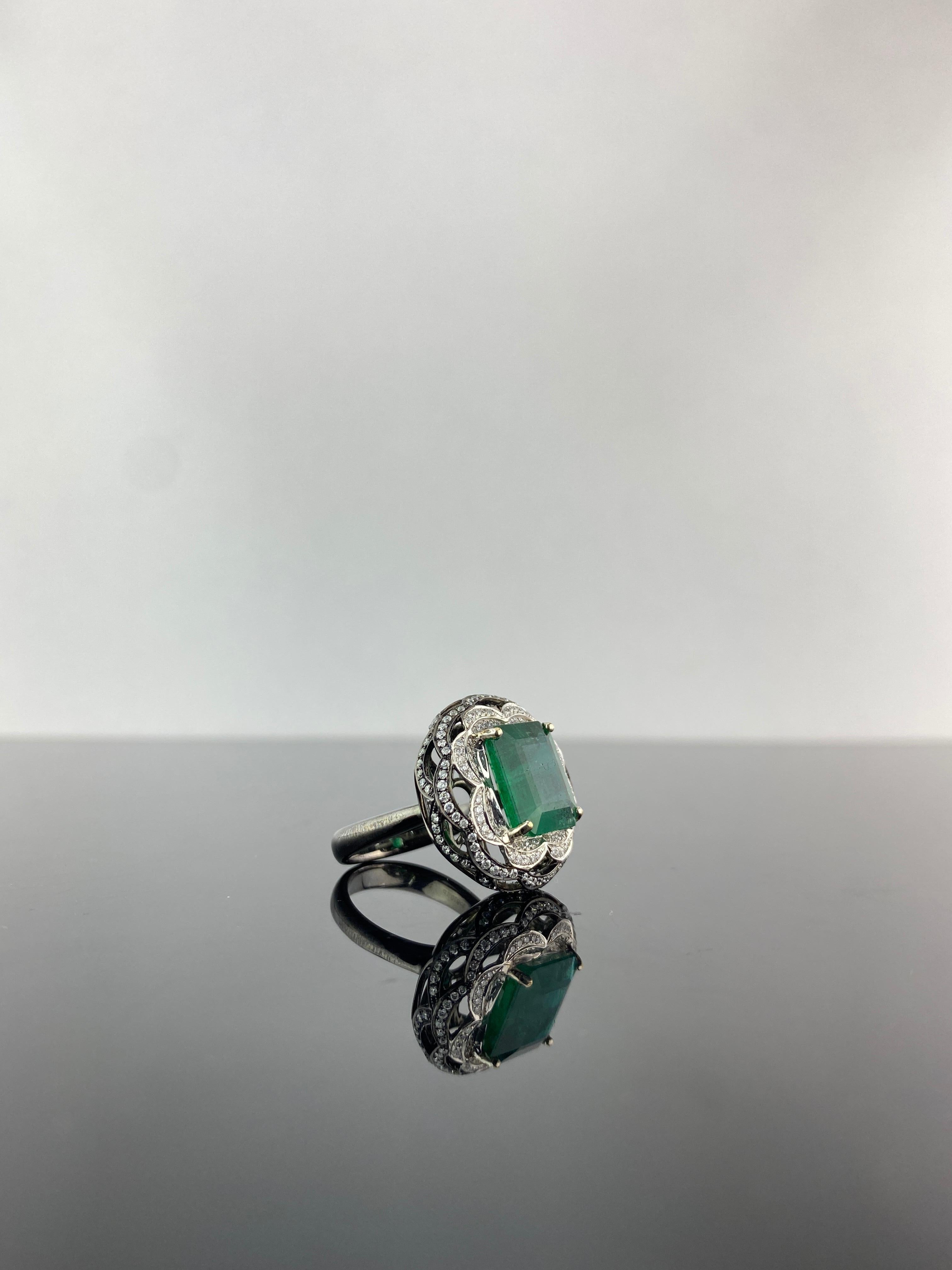 A very unique 18K Black Rhodium and White Gold cocktail ring, with a natural 6.54 carat natural Zambian Emerald center stone and White Diamonds. The Emerald is of high quality, ideal vivid green color and great luster. The ring is currently sized at