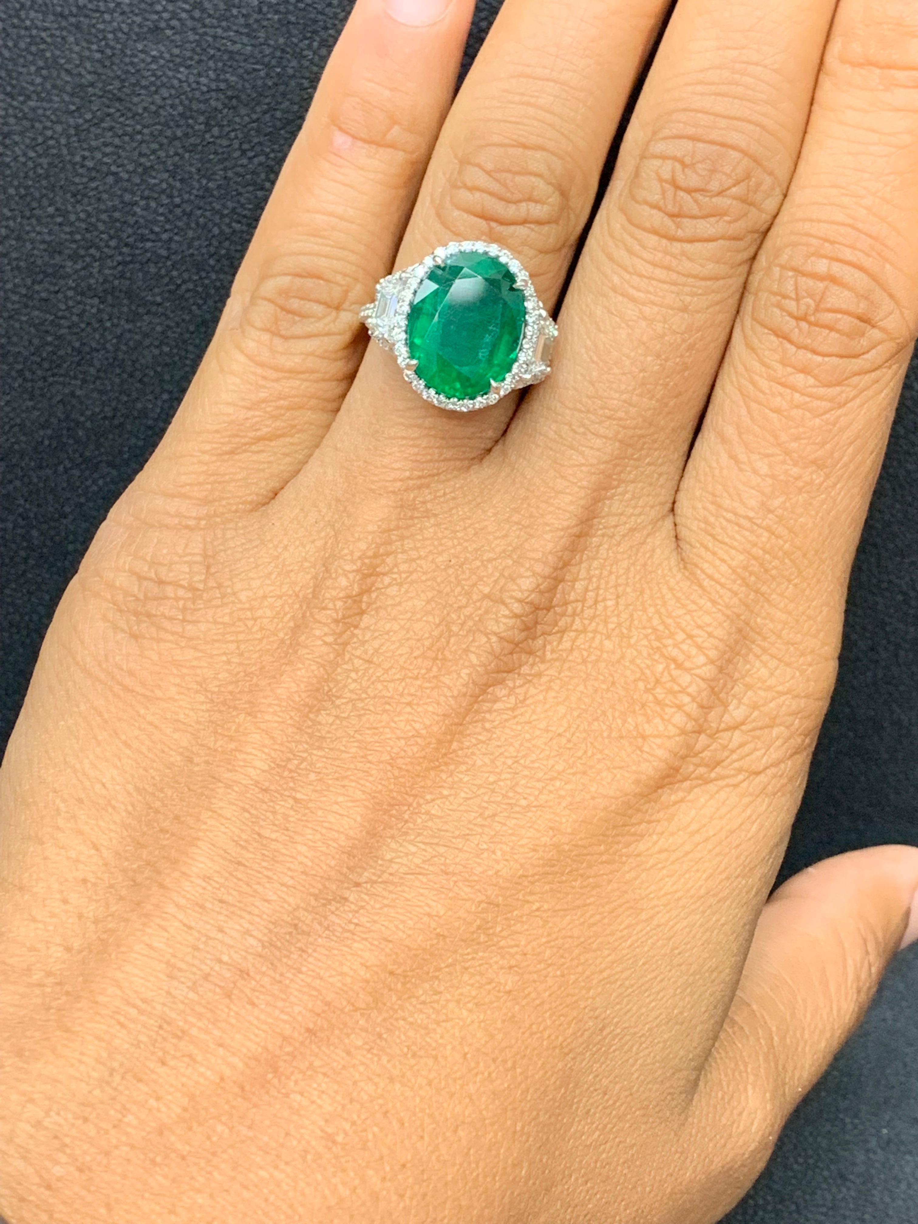 This three-stone ring is set with a 6.55 carat cushion cut emerald center stone flanked with trapezoid diamond side stones weighing 1.14 carats. A single row of round brilliant diamonds accent the center and side stones. Made in platinum . Size 6.5