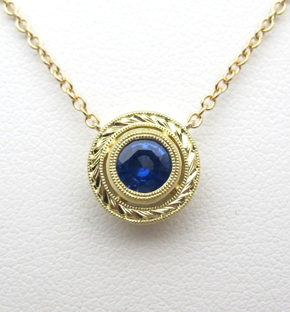 This beautiful necklace features a deep, velvety, royal blue sapphire. It measures 5.33 millimeters in diameter and weighs .66 carats. It is set in a handmade, 18k yellow gold setting that was made by our Master Jewelers in Los Angeles. The piece is