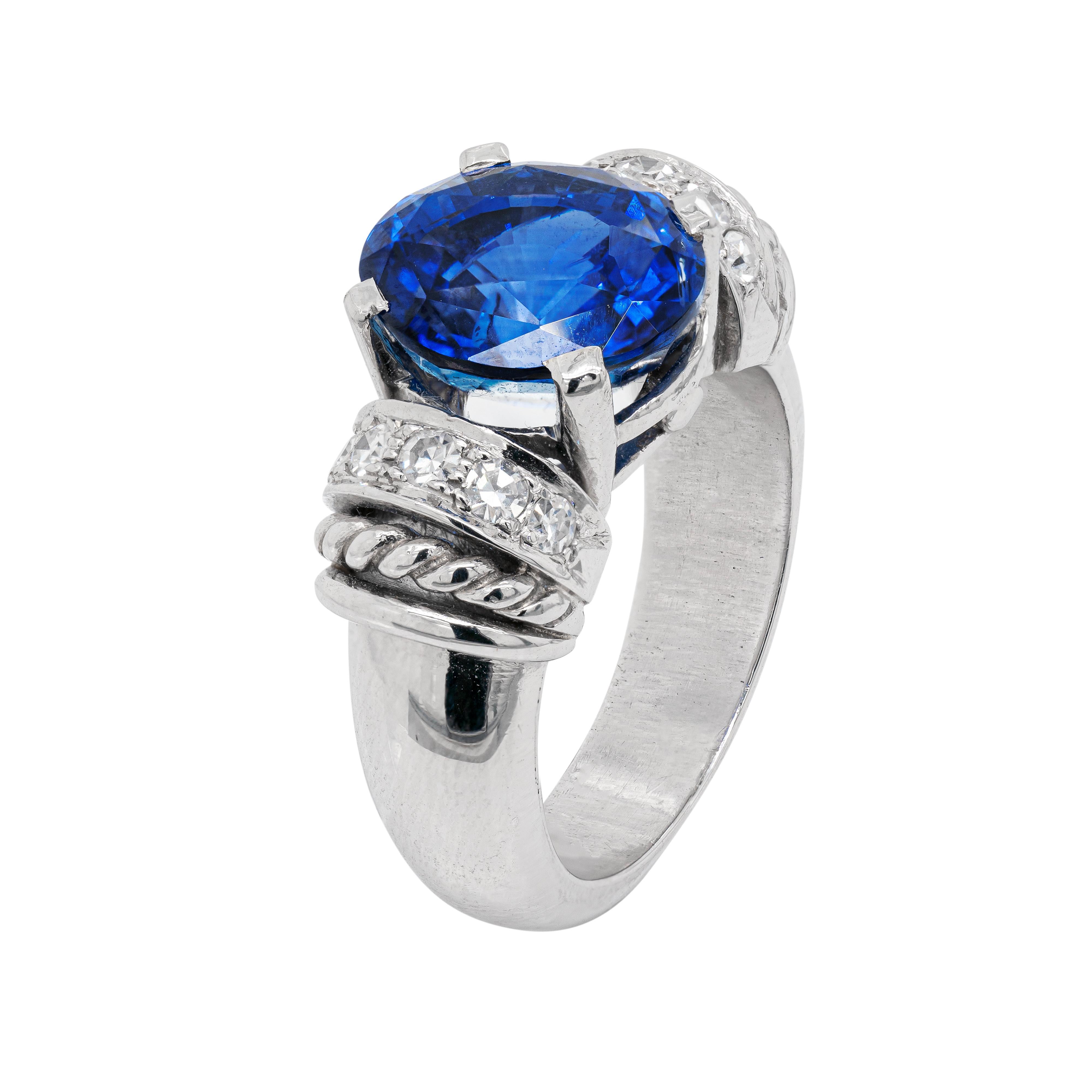Cette merveilleuse bague en platine présente un saphir ovale bleu royal impressionnant pesant 6.60ct, monté dans une monture à quatre griffes, à dos ouvert. La pierre précieuse vibrante est magnifiquement accompagnée de cinq diamants ronds de taille