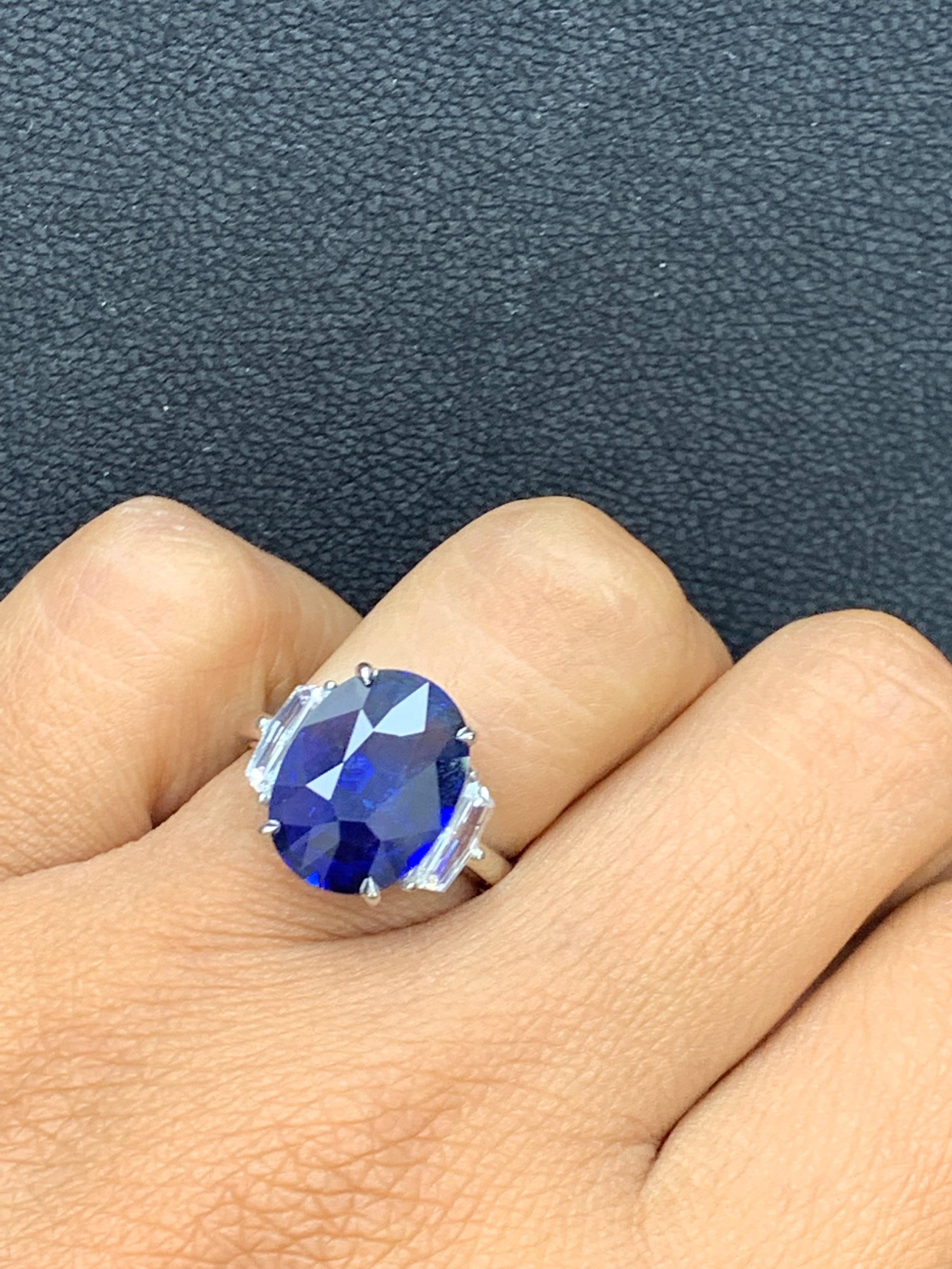 This three-stone ring is set with a 6.61-carat oval cut Vivid Blue Sapphire center stone flanked with step-cut trapezoid diamond side stones weighing 0.59 carats. Made in platinum. Size 6.5 US (sizable).