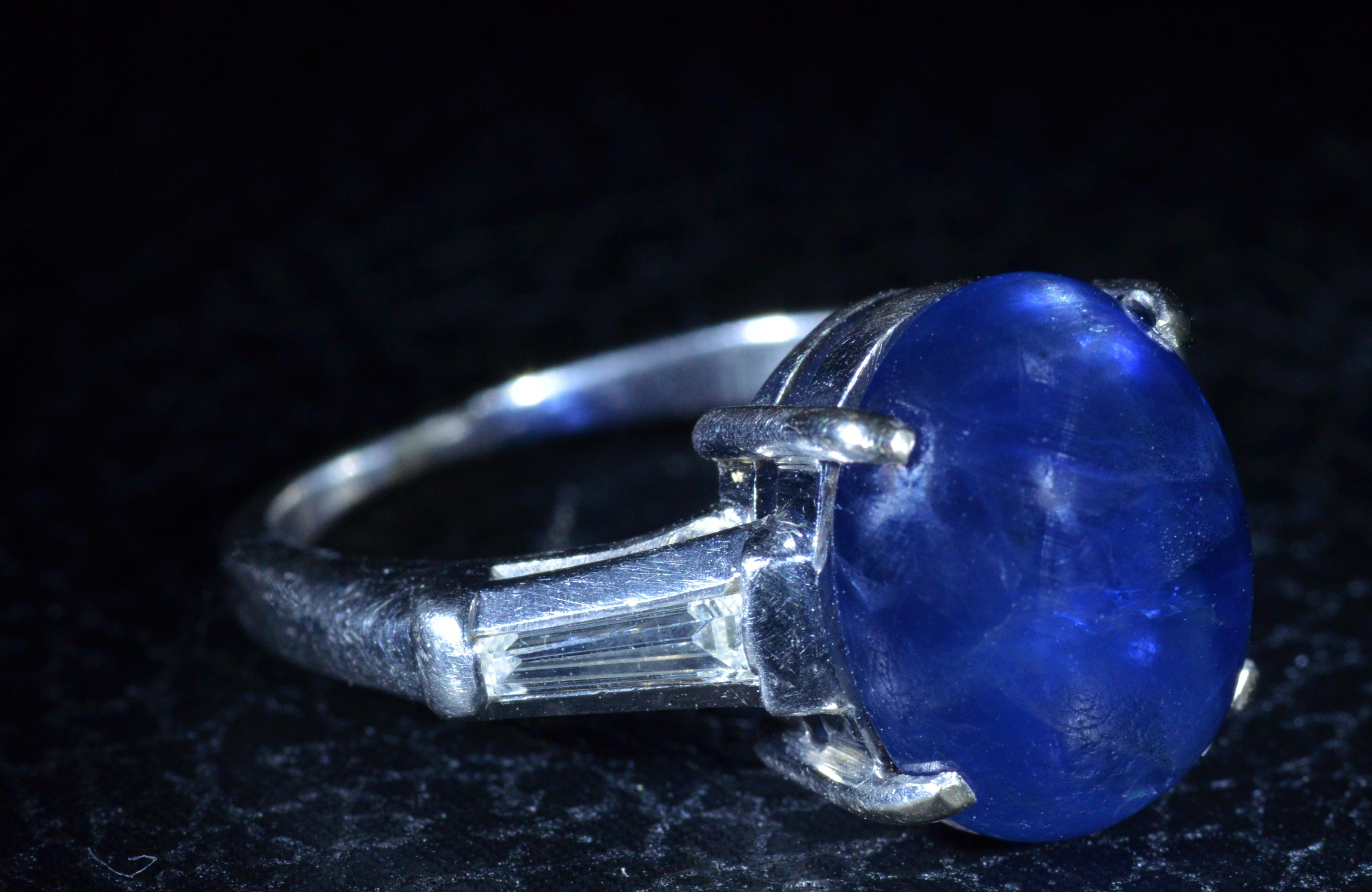 Ladies 6.62 Carat Cabochon Sapphire Ring in Platinum.  On either side of the violetish-Blue sapphire is a single tapered baguette with an approximate total weight by measurement of 0.30 carats. 