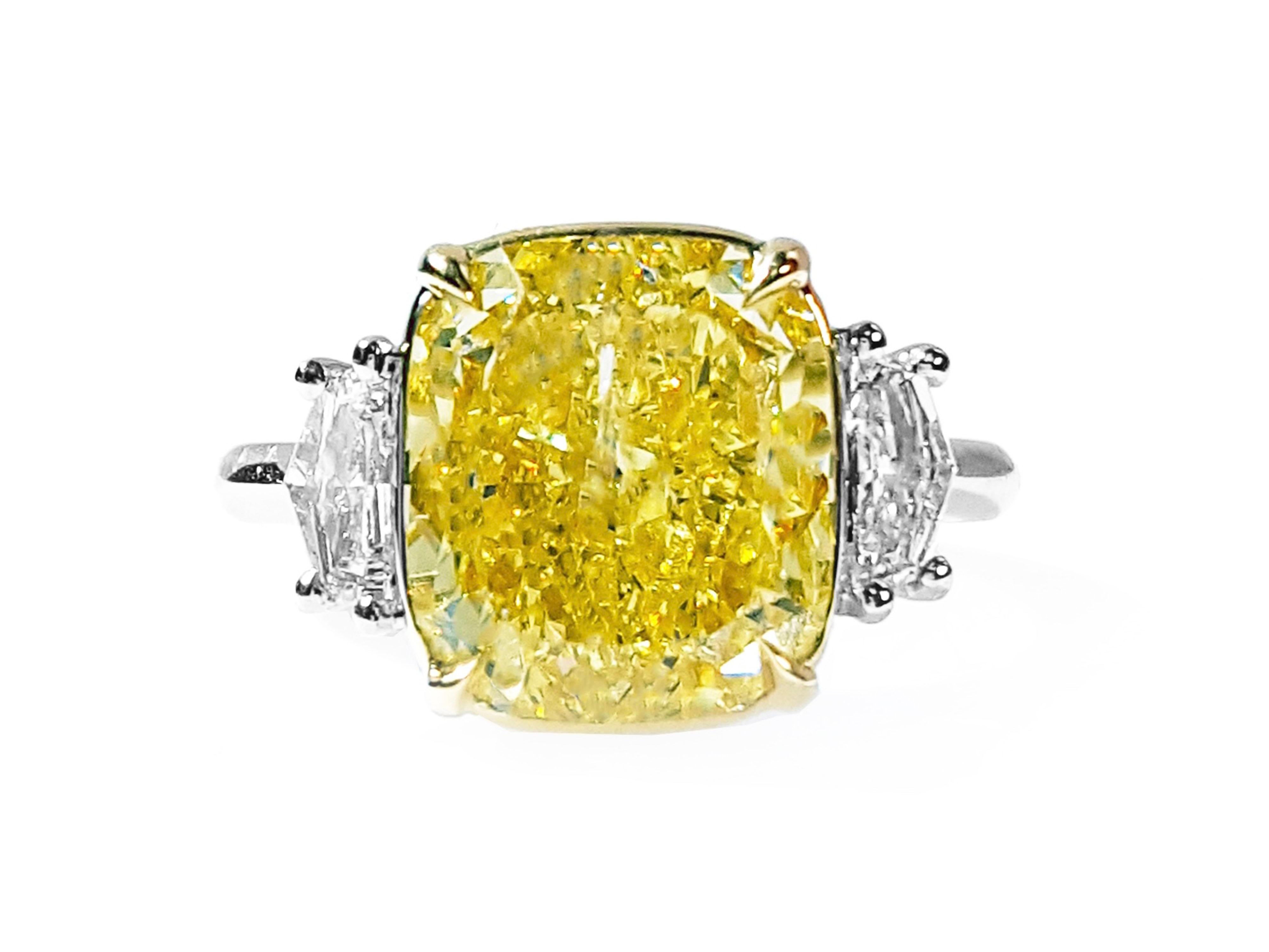 This absolutely stunning engagement ring Three-Stone style showcasing a Fancy Intense Yellow 6.67 carat Cushion cut diamond that has been certified by GIA. Flanked by two Cadillac cut diamonds total weight 0.48 carat, D color, VS clarity. The