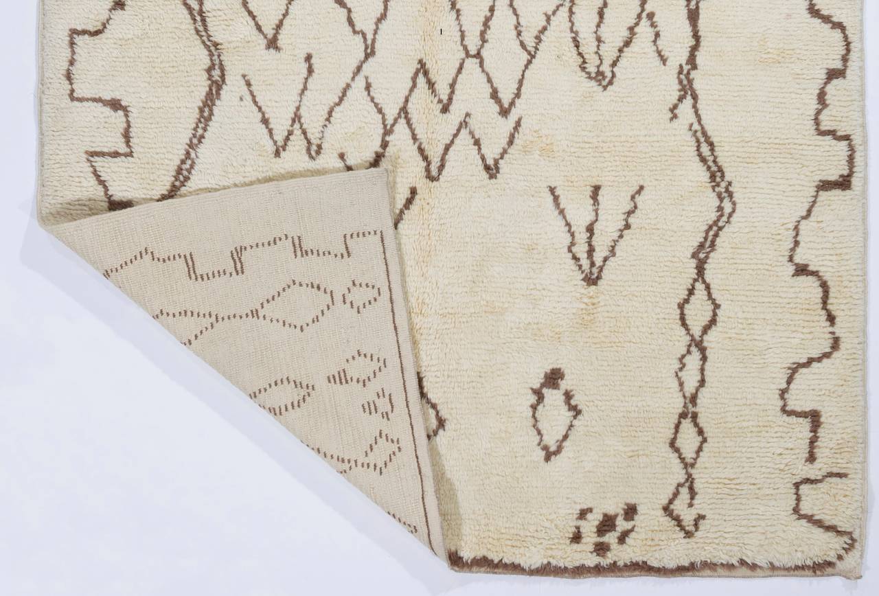 Ein moderner handgefertigter Teppich aus natürlicher, ungefärbter elfenbeinfarbener und brauner Schafwolle. Das Design ist an alte marokkanische Teppiche angelehnt.
Je nach Größe benötigen 3 Knüpfer etwa 5 Wochen, um einen dieser Teppiche von Grund