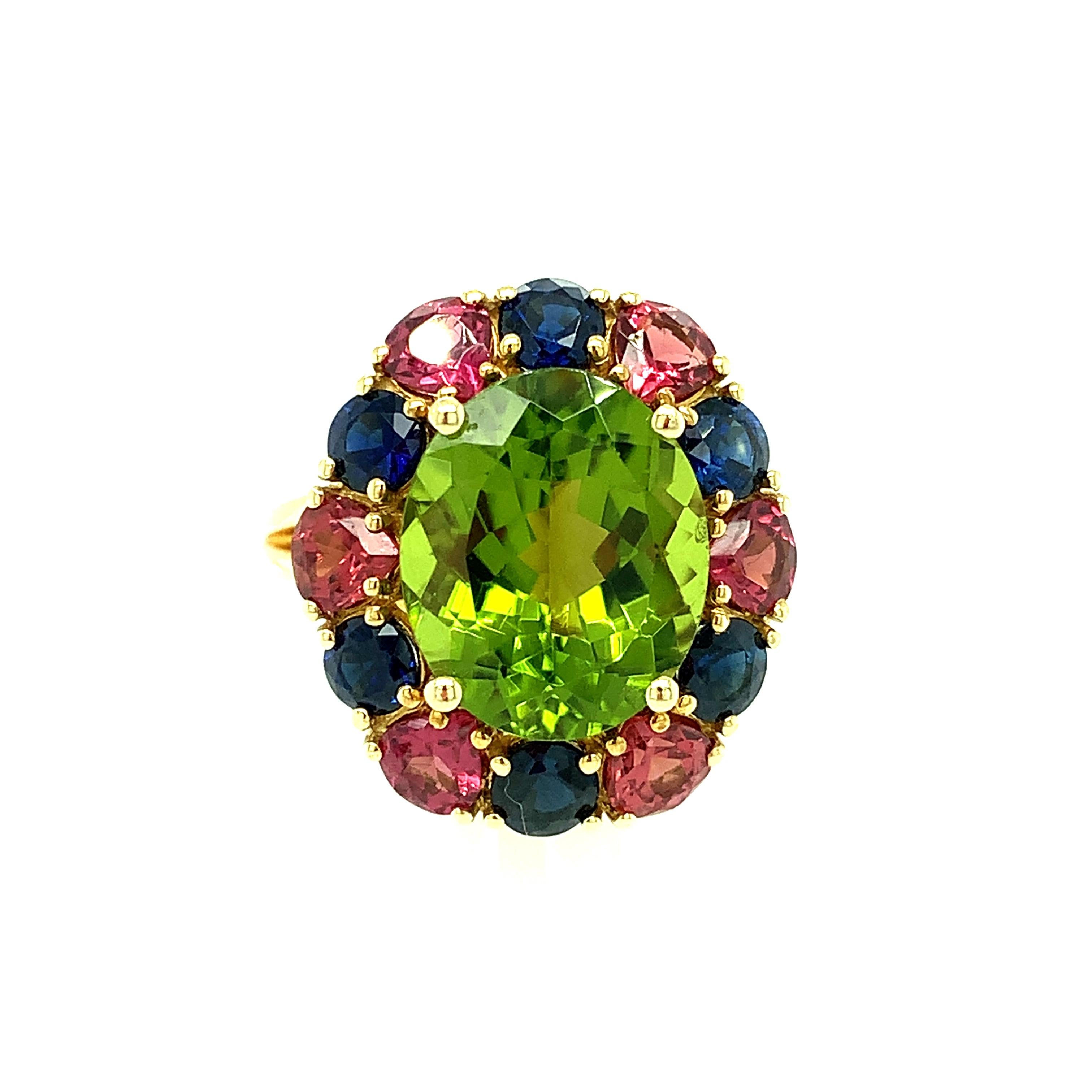 This stunning 18k yellow gold cocktail ring features a velvety, 6.70 carat citrus-green peridot surrounded by a halo of royal blue sapphires and rose colored garnets. Our company was one of the first to combine colors that had rarely been seen