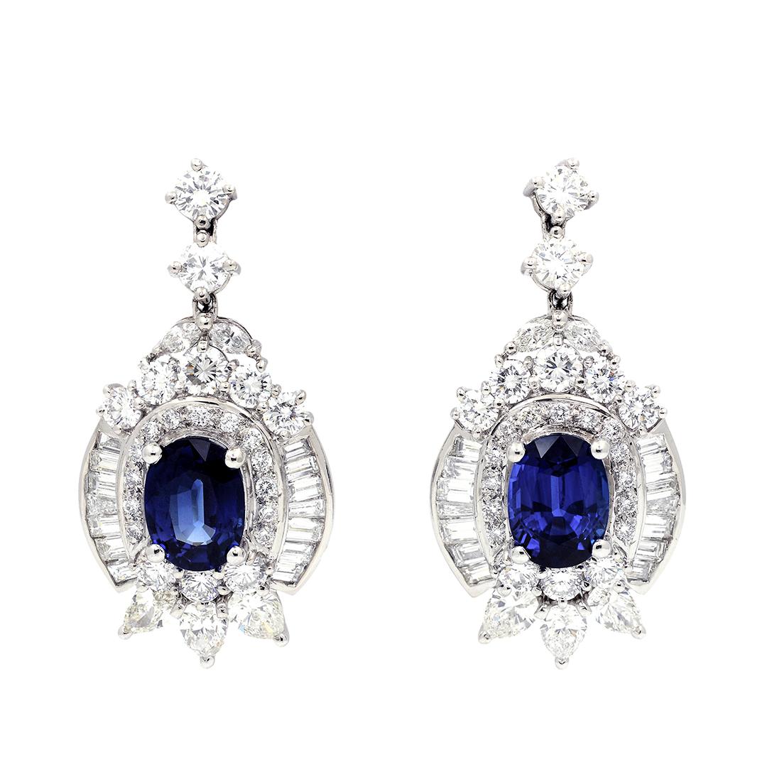 These stunning earrings feature oval blue sapphires at their center with an approximate weight of 6.75 carats. Topping off the elegant vintage design is a mixture of 44 round brilliant, 28 baguette, four marquise, and six pear shape diamonds which