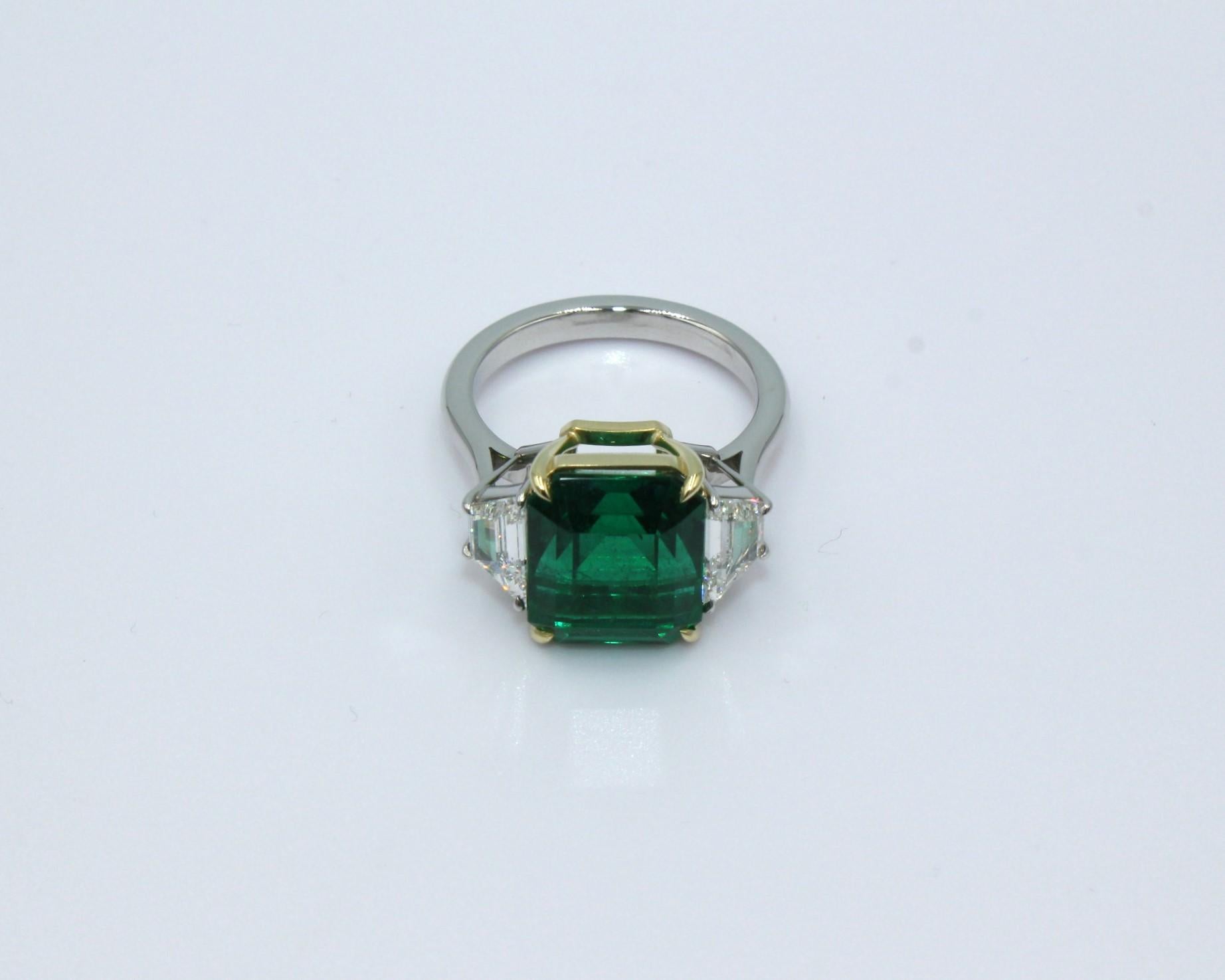 6.75 carat emerald-cut Zambian Emerald with 2 trapezoid shaped diamonds, totaling a diamond weight of 1.06 carat. 

This stunning Emerald & Diamond Ring will highlight your elegance and uniqueness. 

Item Details:
- Type: Ring
- Metal: 18K Gold &