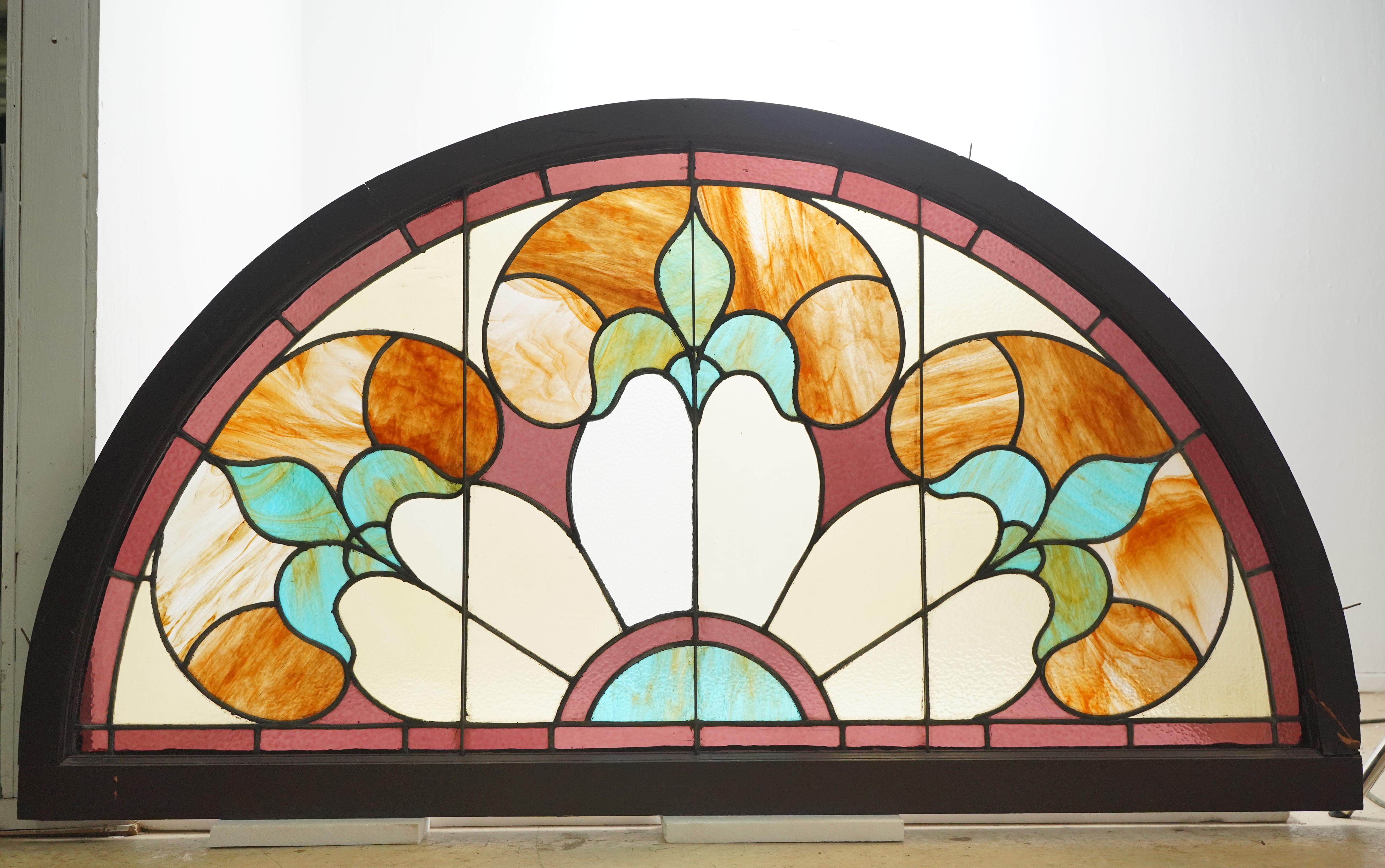 Reclaimed arched window with textured stained-glass panels of yellow, amber, brown, and blue colors. This window is the top piece that was part of an arrangement above two rectangle windows. It was acquired from a church built in 1904 in