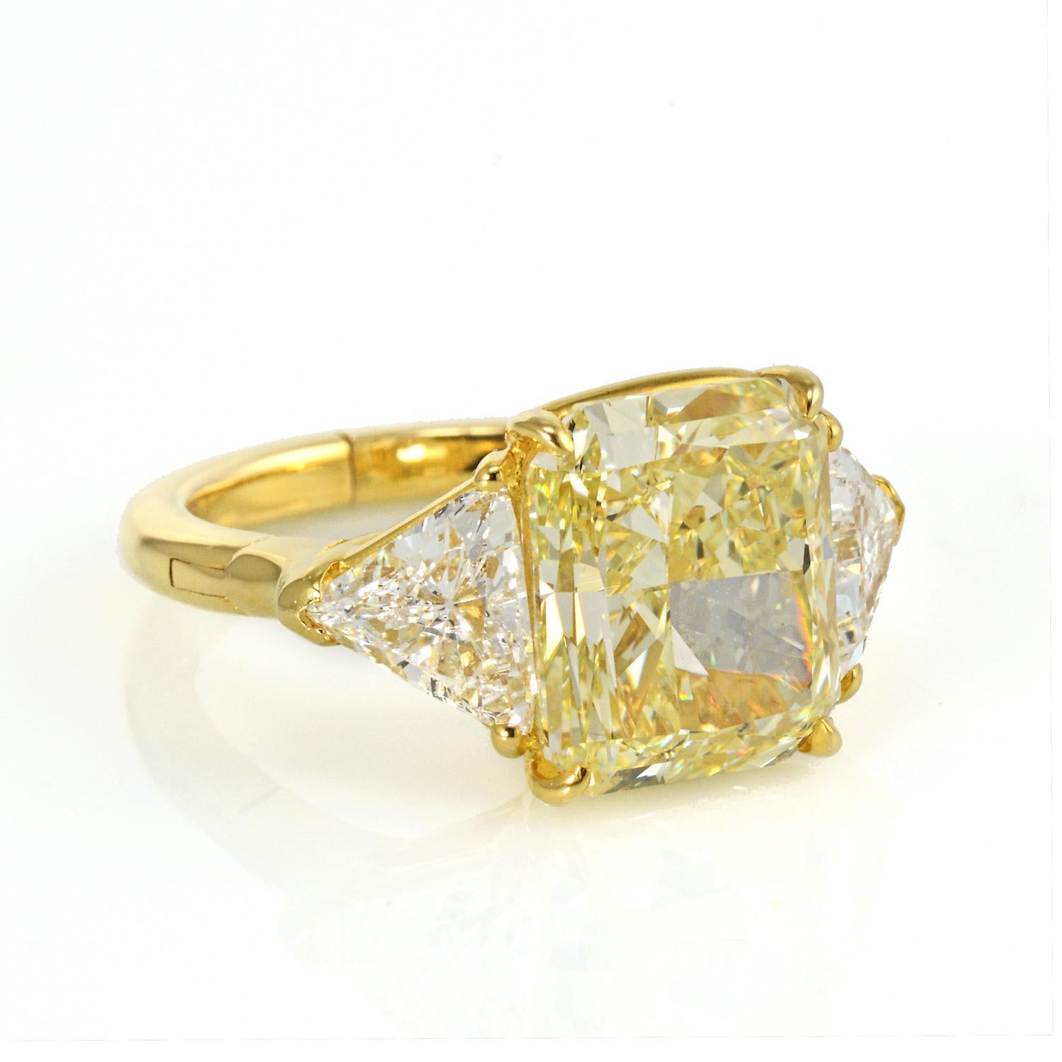 This 6.76 ct natural color Radiant Cut Fancy Yellow Diamond (VVS2) is flanked by 2 colorless Trillion Cut Diamonds, all set together in a beautiful three stone diamond engagement ring. Crafted in 18K Yellow Gold together three diamonds make a really