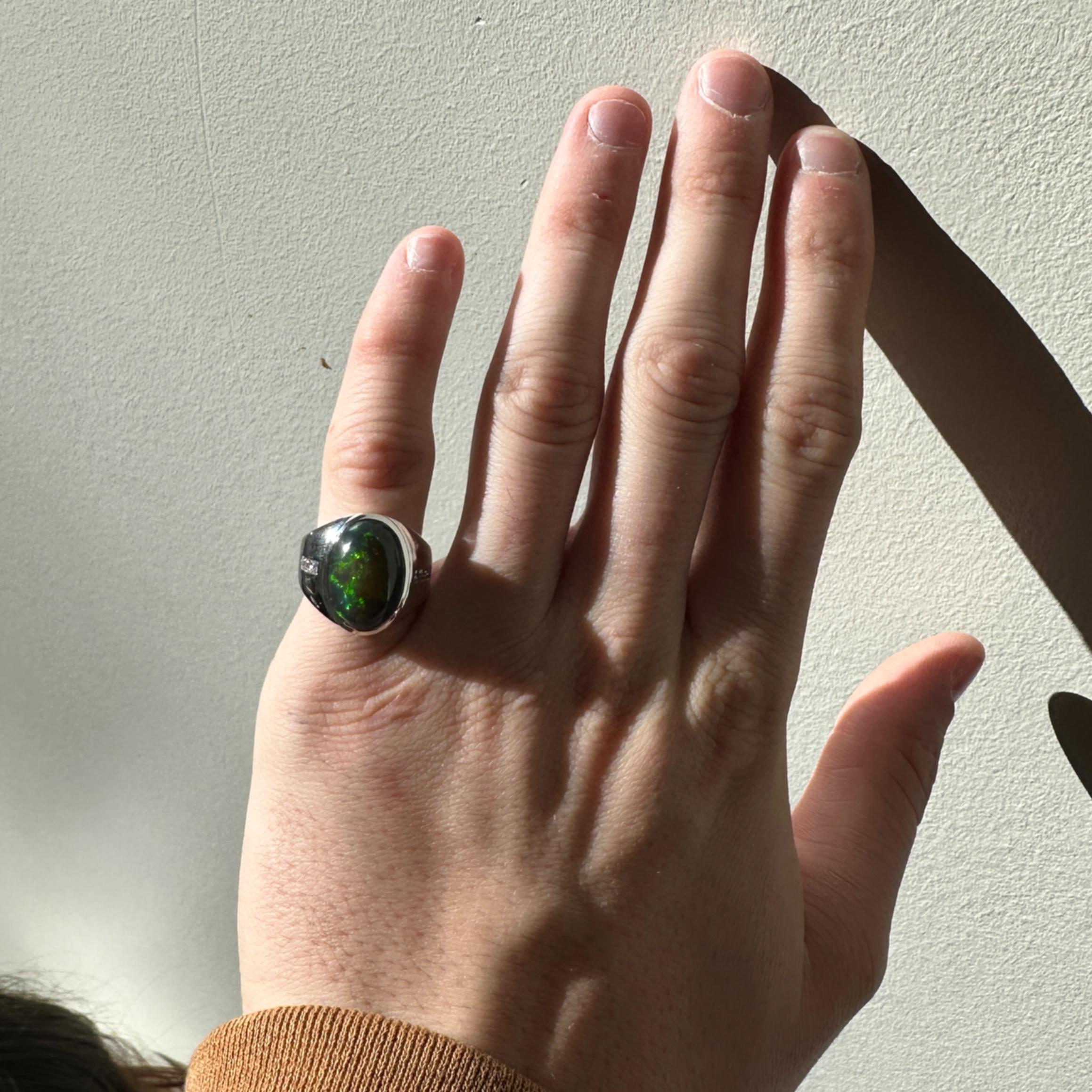 This statement men's ring features a 6.68 carat oval black opal gemstone of size 16x11mm with a halo of natural earth mined diamonds, all set in solid 14K white gold. This ring can be a beautiful October birthstone gift for your loved ones!

**We