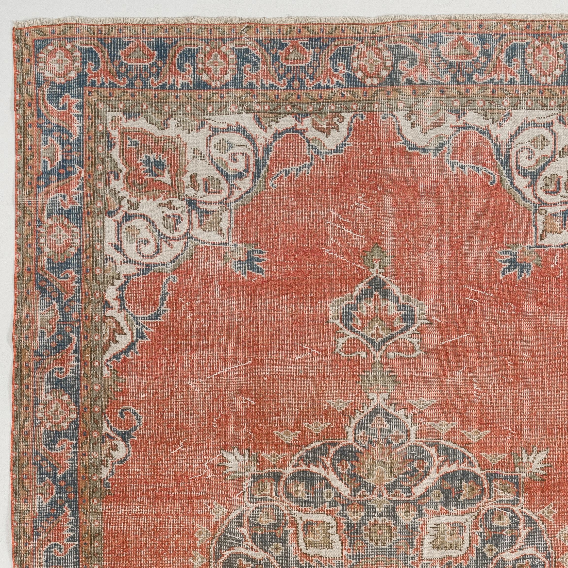 A fine vintage hand knotted Turkish Oushak rug from the 1960s featuring a central floral medallion in faded navy blue against a plain warm madder red field, finished off with spandrels in cream and a border in olive green and navy blue both filled