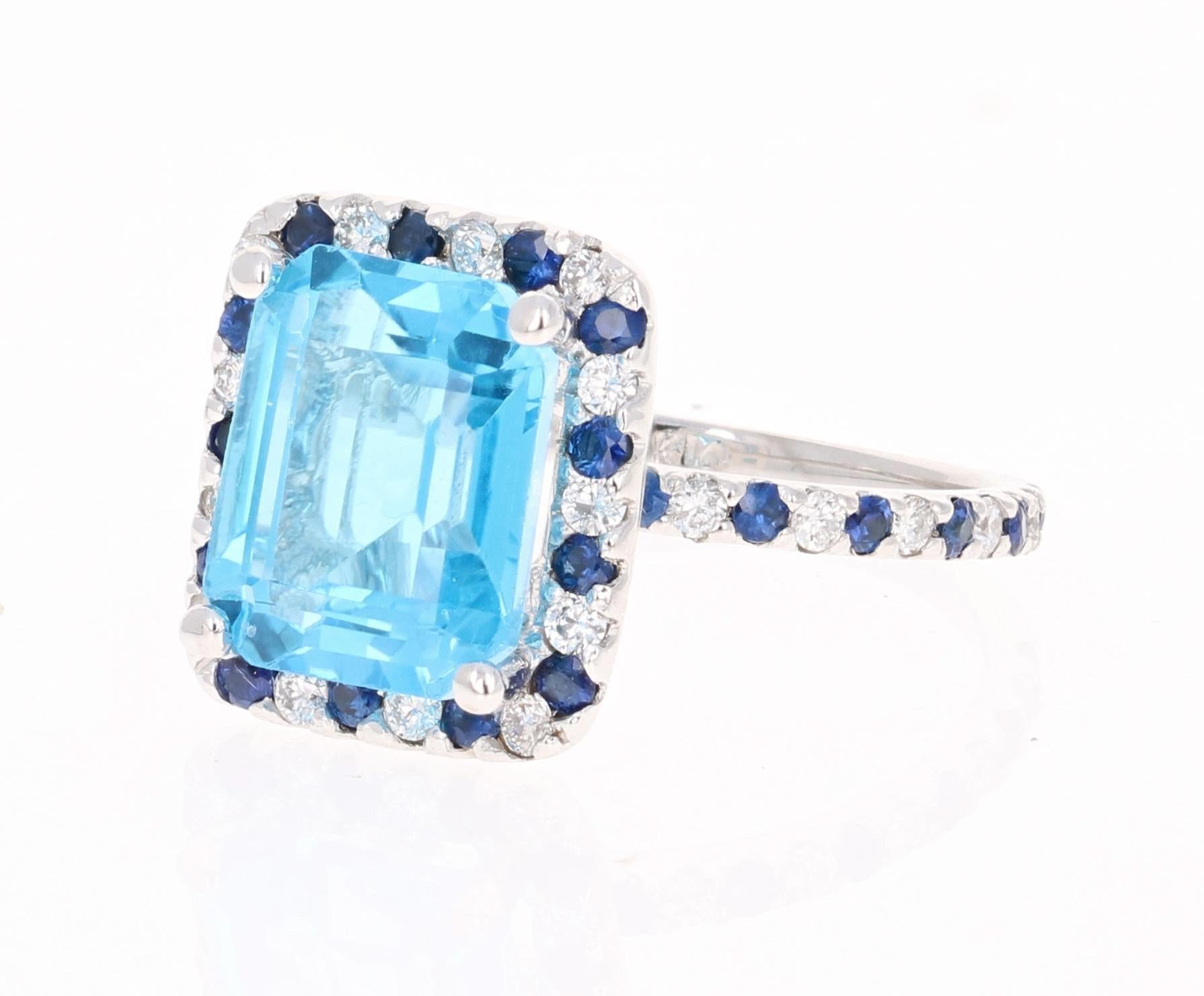 Beautiful to say the Least! This magnificent Emerald Cut 5.90 Carat Blue Topaz is surrounded by 24 Round Cut Diamonds that weigh 0.42 Carats (Clarity: SI, Color: F) and 24 Blue Sapphires that weigh 0.51 Carats. The total carat weight of the ring is