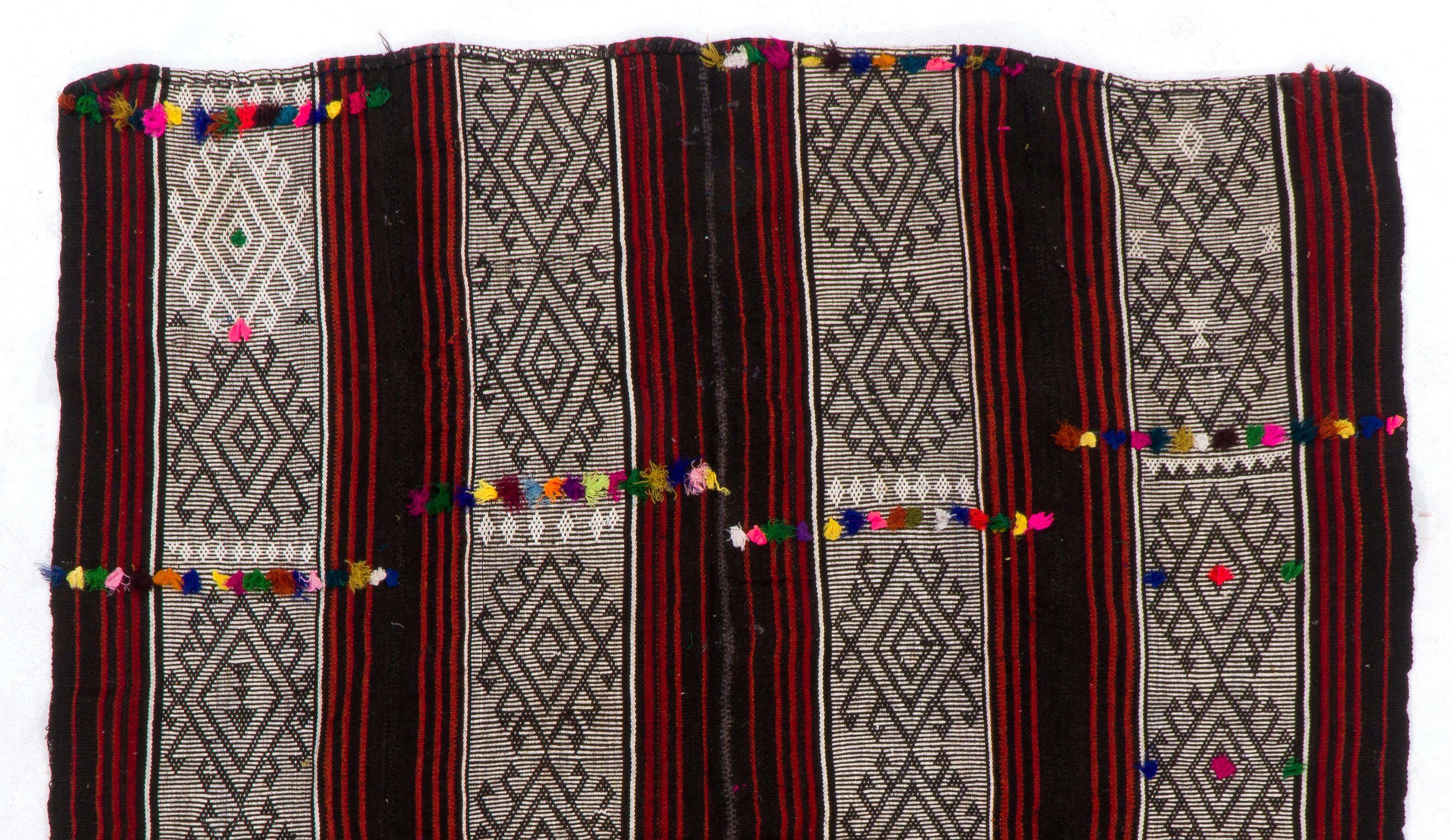A vintage handwoven flat-weave (kilim) from Turkey made of cotton and wool featuring a 'boho chic' design with colorful pom poms on a field with vertical stripes and burdock motifs in red, very dark brown and cream colors. Ideal for both residential