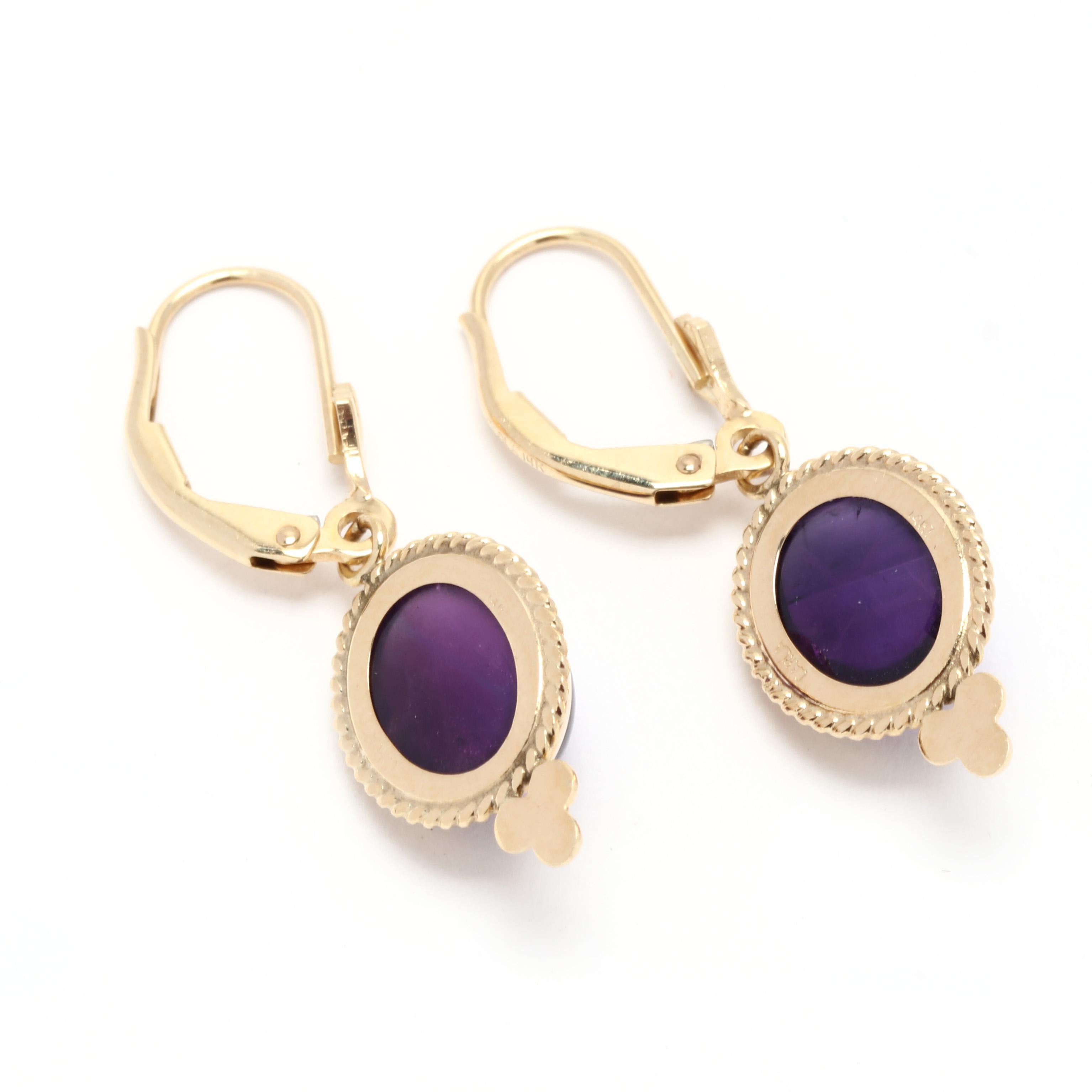 A pair of vintage 14 karat yellow gold cabochon amethyst dangle earrings. These February birthstone earrings feature bezel set, oval cabochon cut amethysts weighing approximately 6.90 total carats with a rope motif halo and suspended from a pierced