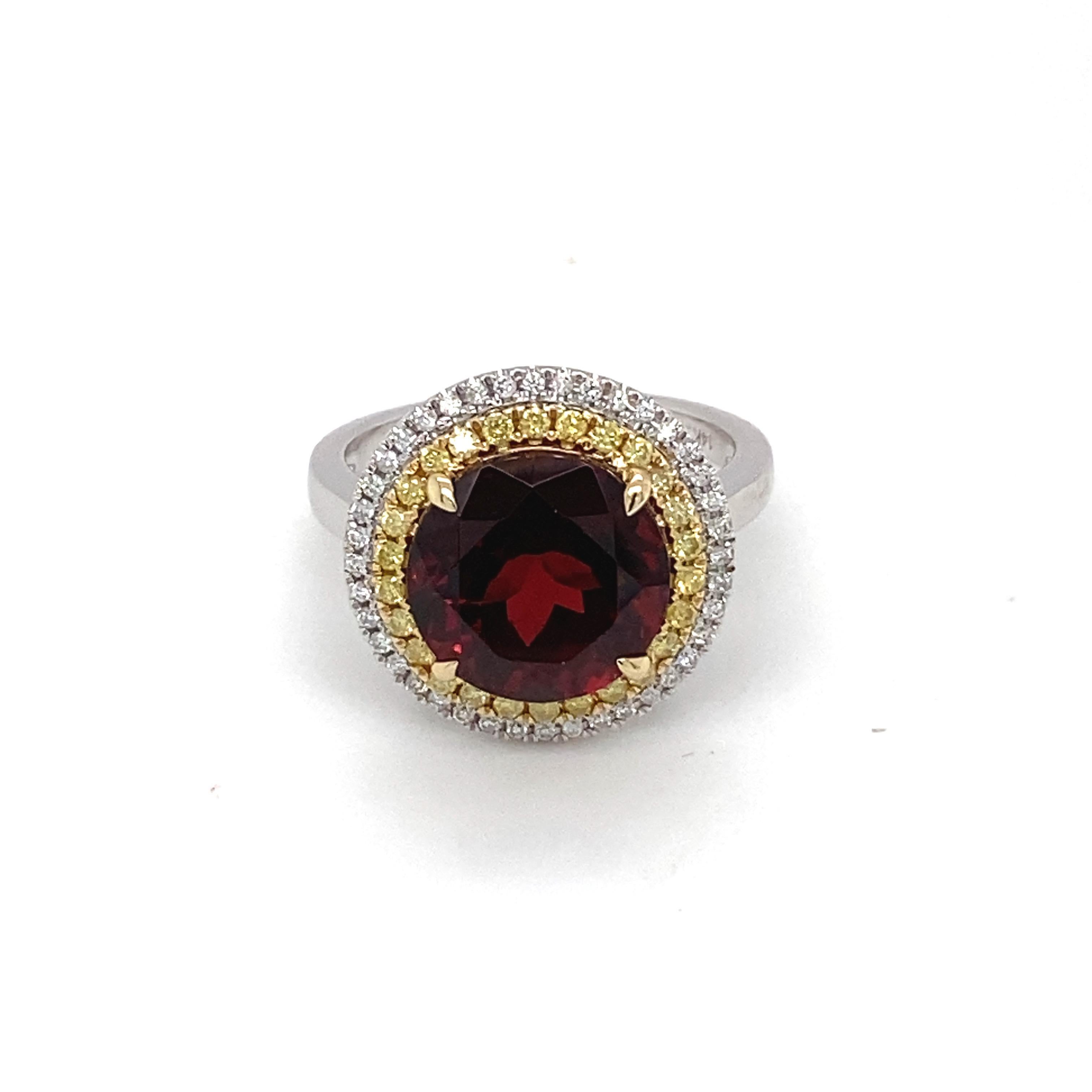 Este elegante anillo con halo de granate presenta una piedra central de granate redondo de 6,97 quilates con un halo doble de diamantes amarillos y blancos de 0,39 quilates engastados en oro de dos tonos de 14 quilates. Es muy adecuado para llevarlo