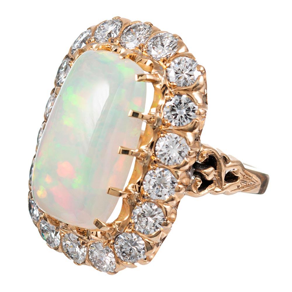 This classically styled cluster ring is centered upon a 6.98 carat opal and framed with approximately 3 carats of brilliant white diamonds. The mounting is made of 14 karat yellow gold and offers ornately styled shoulders. The piece has a striking