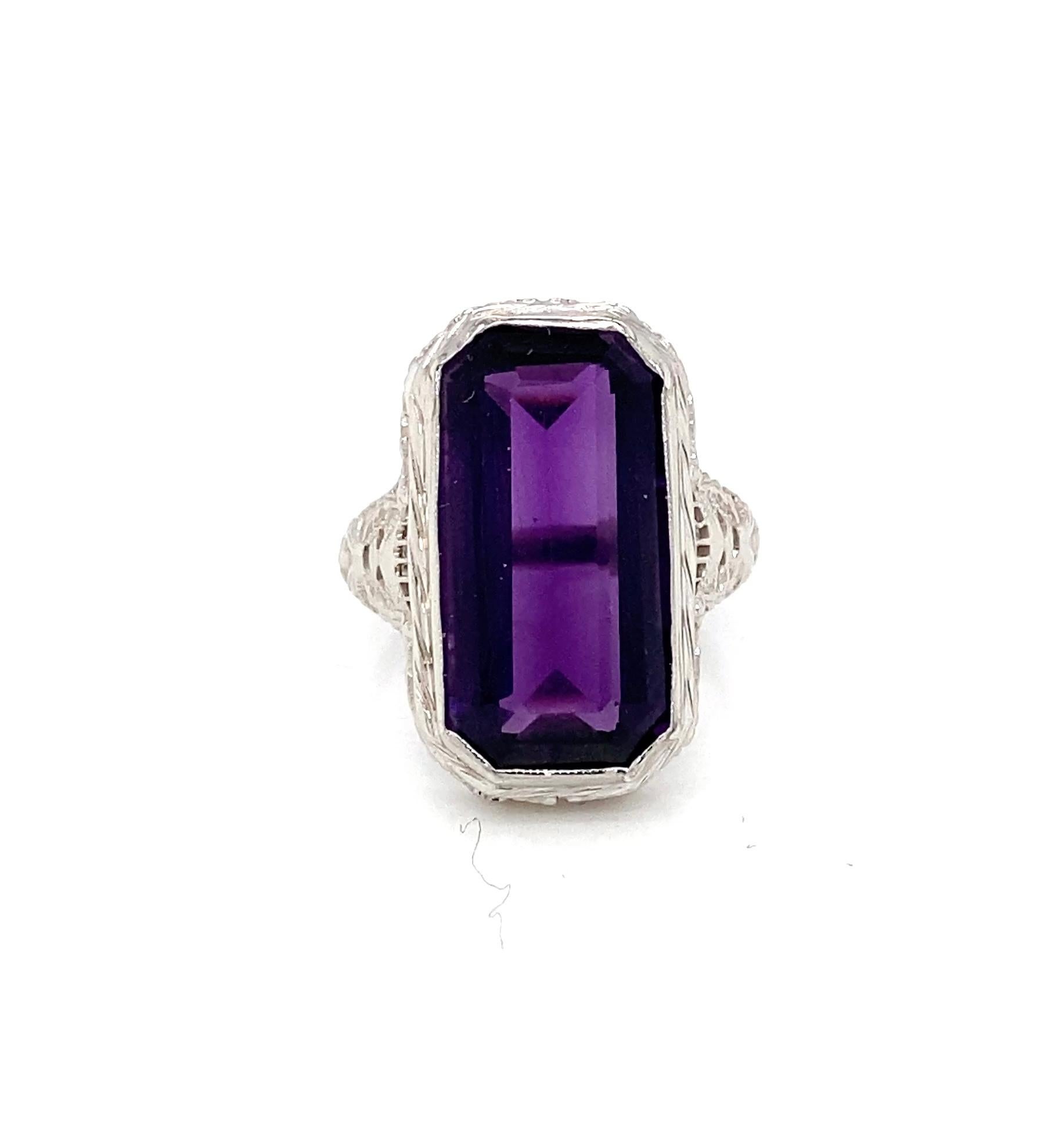 One Art Deco 1930s 14 karat white gold ring centered with a striking emerald cut amethyst weighing approximately 6.99 carats. The amethyst displays a vivid and luminous purple hue, enhanced by the clean step-cut facets that allow light to reflect in