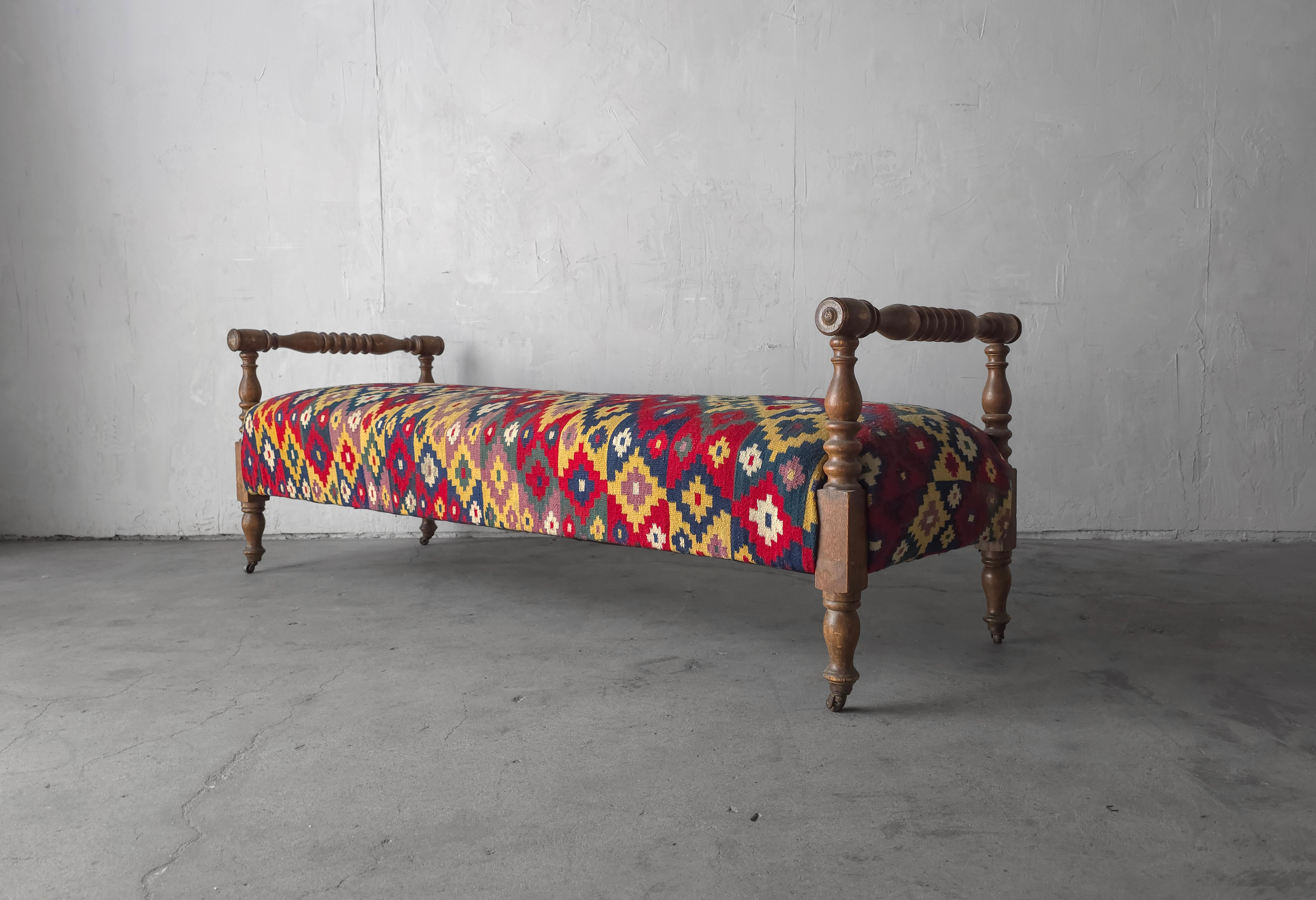 Questa grande panca è uno splendido pezzo d'antiquariato autentico con tutti gli ambiti dettagli del genere.  I fusi torniti a mano, le mini rotelle e la splendida patina del legno, il tutto vestito con una splendida e antica tappezzeria Kilim
