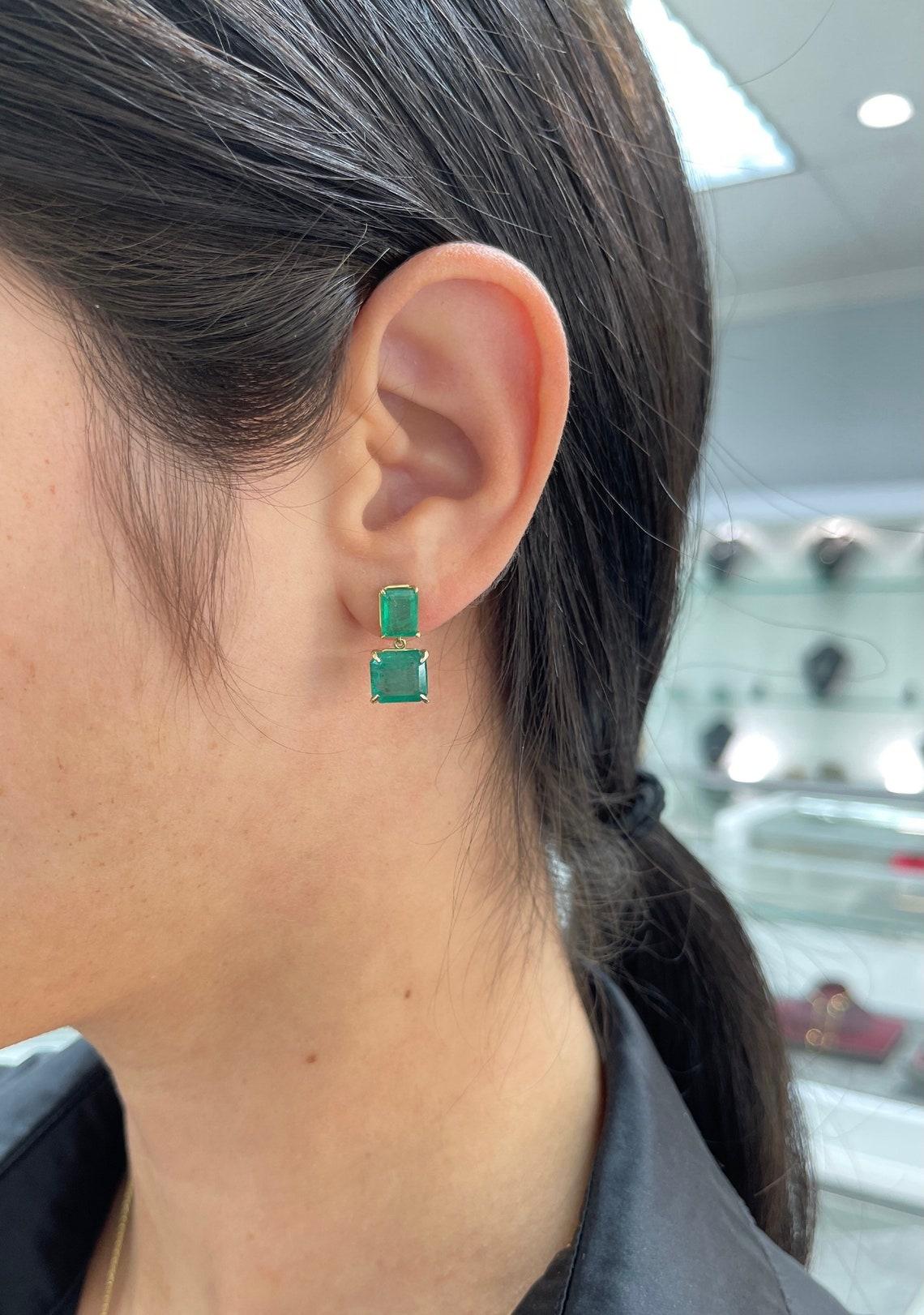 A pair of fine investment quality luxurious dark Emerald dangling studs in fine solid 18K yellow gold. Displayed are dark luscious green natural emerald cut, emeralds with very good transparency, fine color, and accented by a simple secure