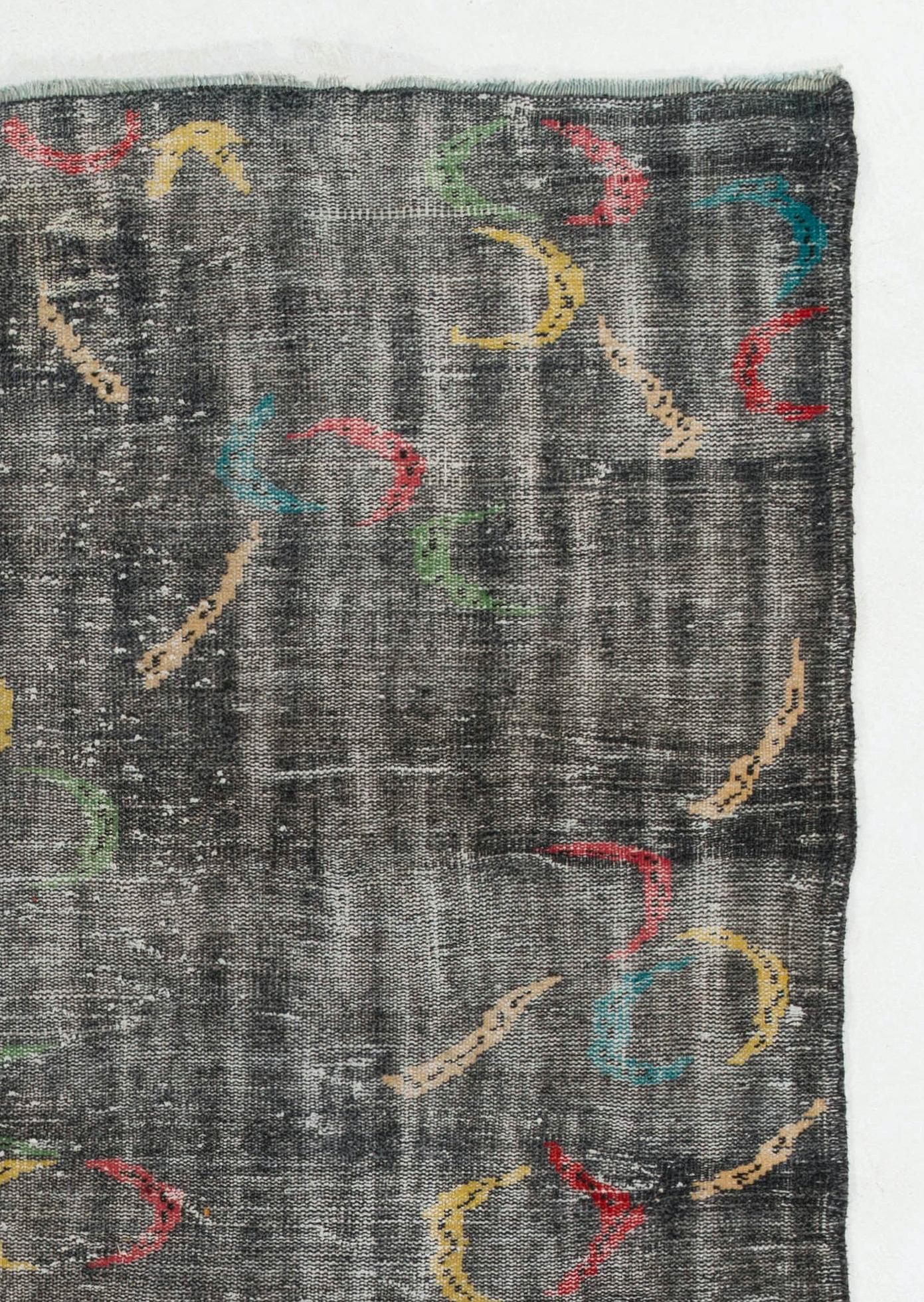 A finely hand-knotted rug made of wool on cotton foundation designed by Zeki Muren. The rug features a design of free-floating boomerang shaped figures in red, yellow, green, teal and beige against a charcoal gray background. 

Distressed rug in