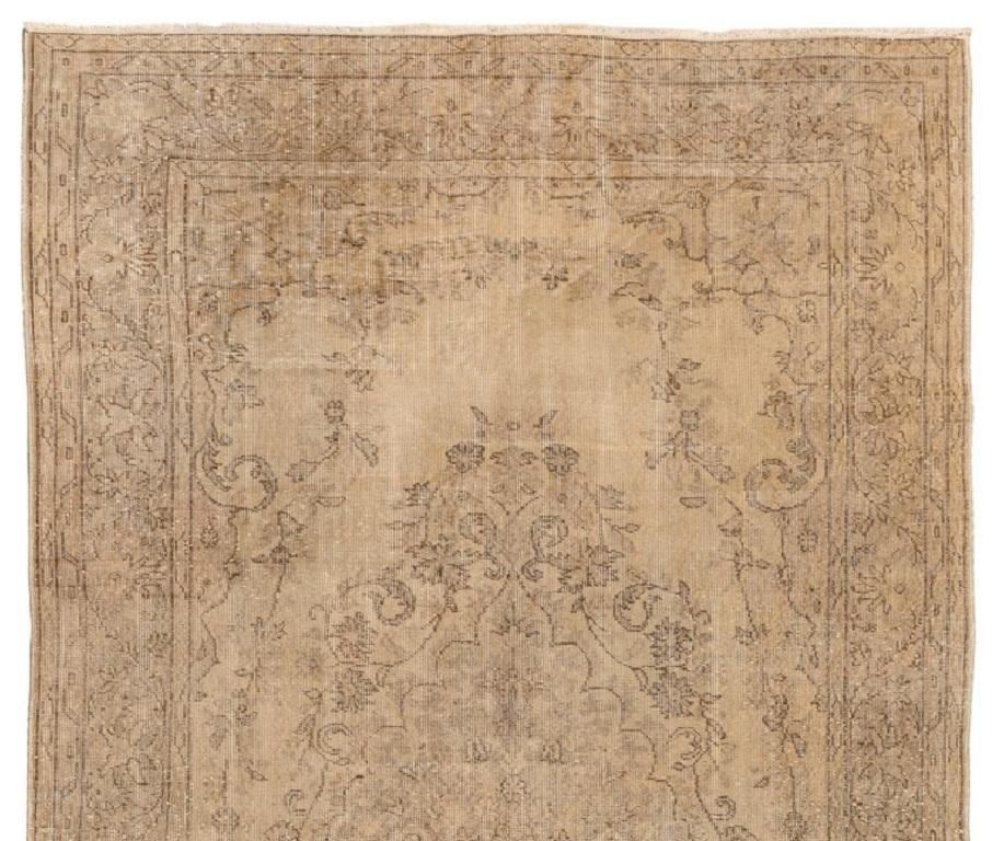 A finely hand-knotted vintage Turkish rug from the 1960s featuring a delicate medallion design decorated all around with lush floral wreaths in brown and taupe gray against a sand beige background. The rug has distressed low wool pile on cotton