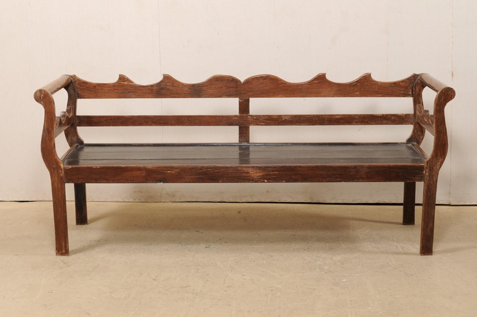 A Brazilian peroba wood bench from the mid 20th century. This vintage wood bench from Brazil features a beautifully carved top rail, reminiscent of waves cresting, with a middle back slat board, horizontally placed at center. Sides are flanked