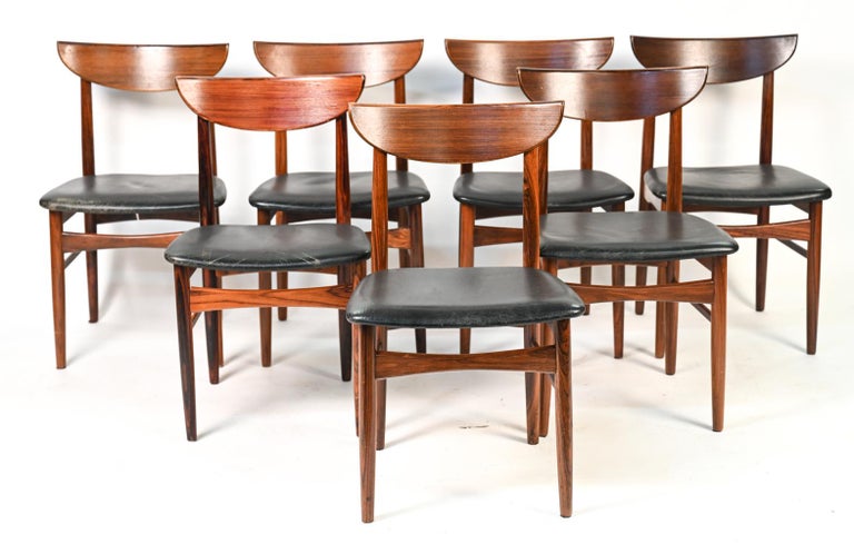 (7) Danish mid-century dining chairs designed by Harry Østergaard for Skovby in handsome rosewood. Featuring black leather seats, elongated crescent bowed backrests.