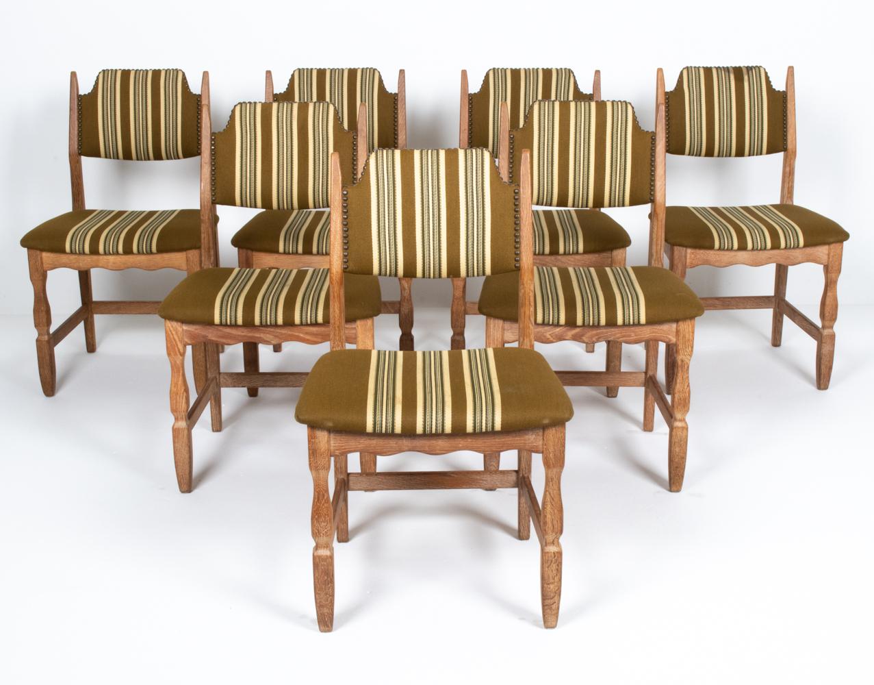 A set of seven Danish midcentury dining side chairs by designer Henning Kjaernulf, well-renowned for his iconic farmhouse-inspired carved oak furniture designs, c. 1960s. These charming Provincial chairs feature low sculpted backs, an upholstered