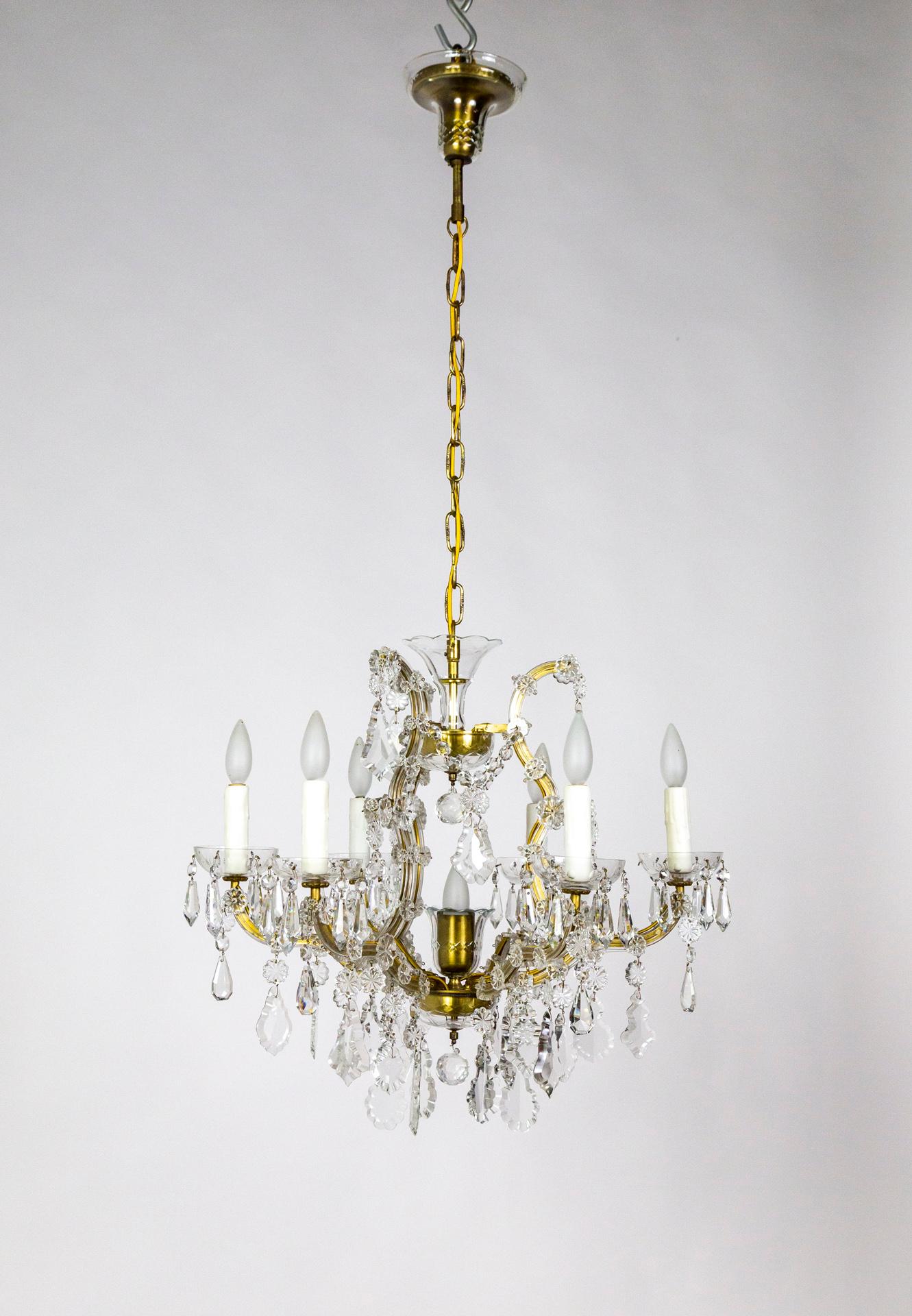 A six-arm, brass and glass chandelier in the Maria Theresa style from the mid-20th century with many large, dangling crystals. It has a center light with a brass socket cover and glass bobeche, echoed in the glass-cupped brass canopy, and six