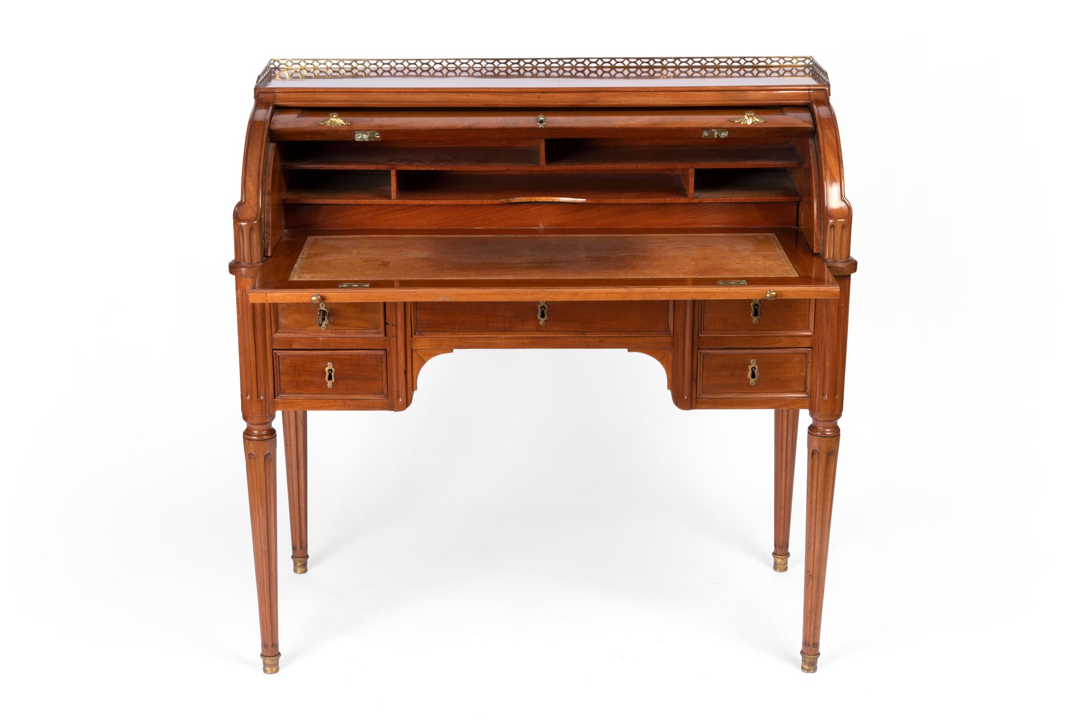 A small but elegant Louis XVI desk in molded mahogany and Caribbean mahogany veneer, engraved and gilded bronze ornamentation, the recess partly surrounded by an openwork gallery, the cylinder revealing five compartments, the border opening with