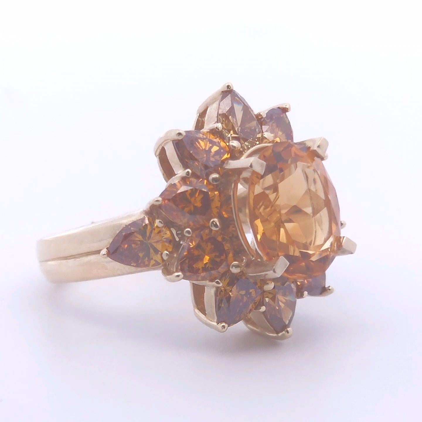 This exquisite 7.ct Citrine and Orange Diamond Ring in 14k Yellow Gold is a true statement piece. At its center, a stunning 3.36ct oval citrine gemstone radiates vibrant, golden hues, capturing the warmth of sunlight. Surrounding this captivating