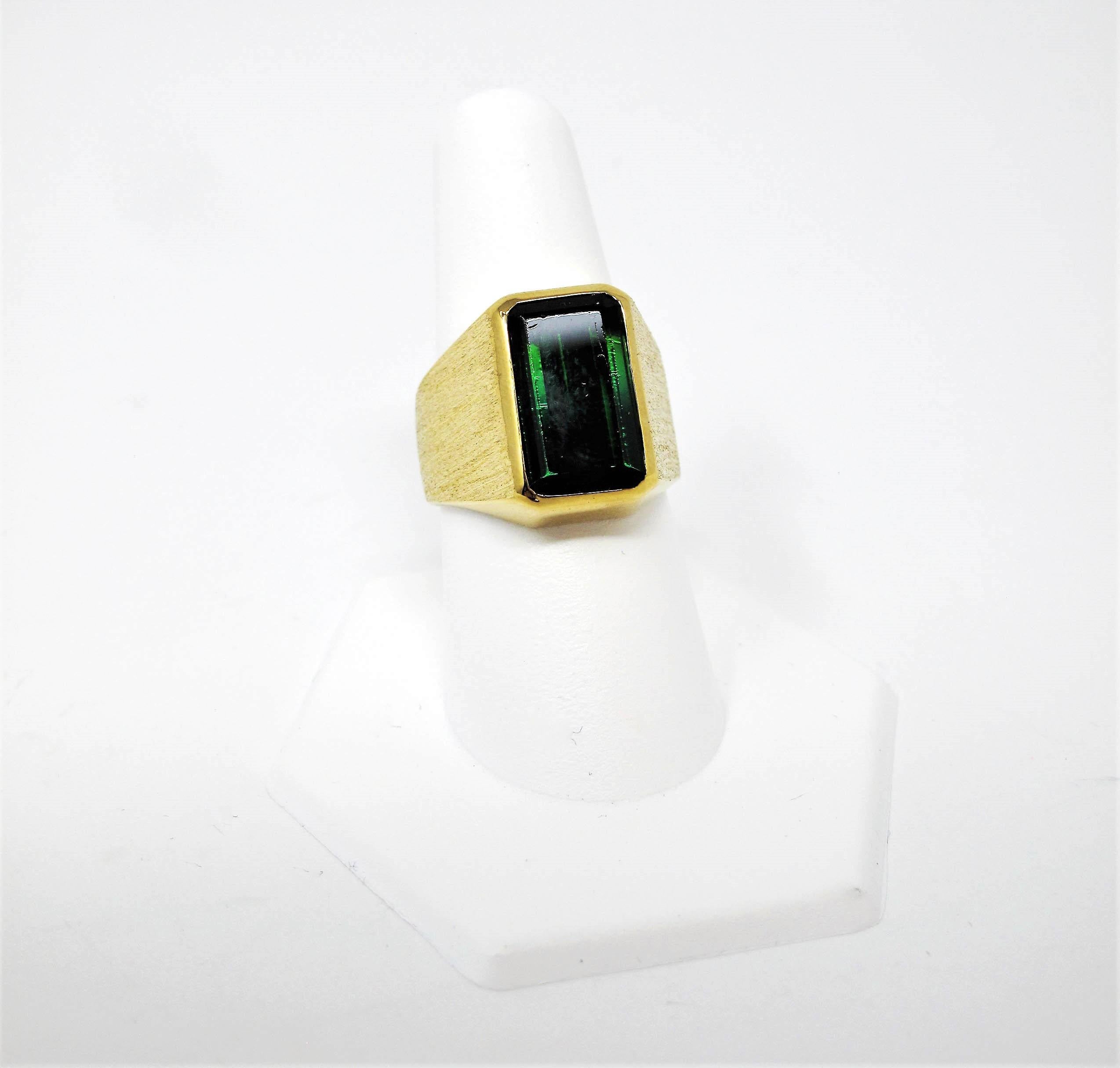 Incredible emerald cut green tourmaline signet style mens ring. This bold, handsome piece is contemporary in composition with its sleek design and clean features. The sizeable green gemstone really pops, while the heavily textured brushed gold band