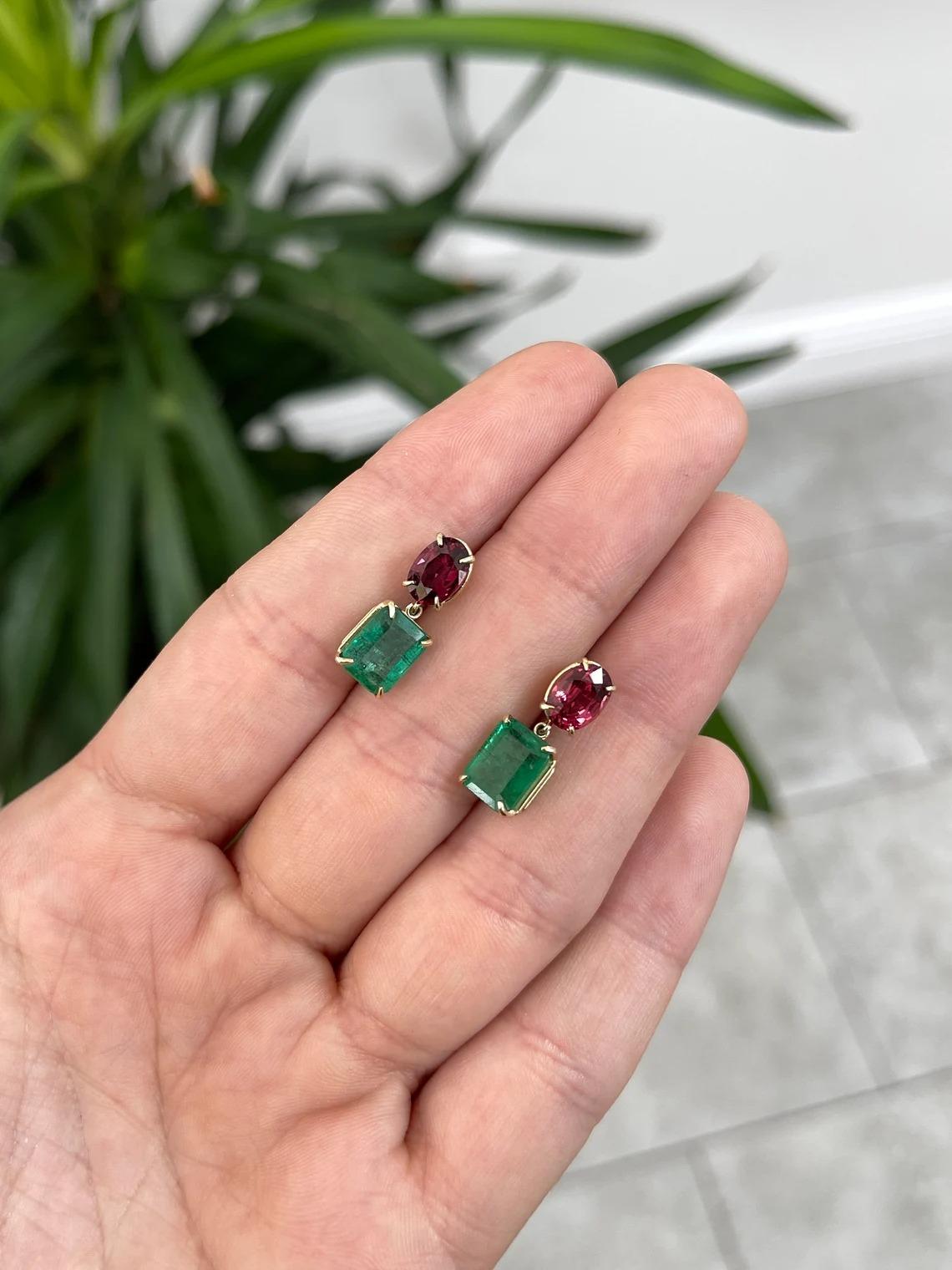 A stupendous pair of natural emerald and spinel dangle earrings. Stunning emerald cut emeralds dangle; showcasing a gorgeous forest green color, very good luster, and good clarity. Accenting above are a pair of sensation natural oval cut spinels