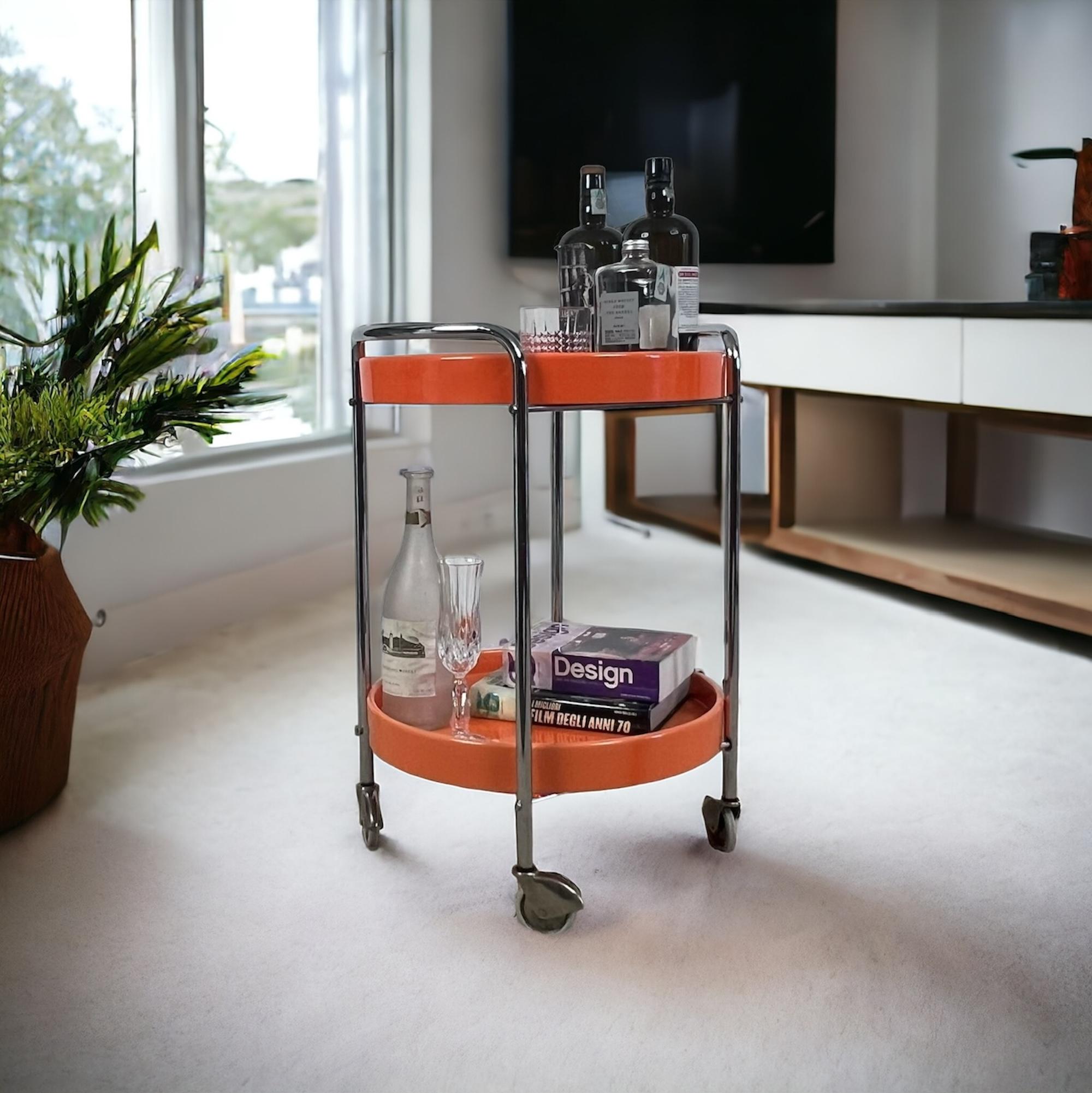 Step back into the vibrant zest of the Seventies with this stunning vintage 70s bar cart, made in Italy. This eye-catching piece features a sleek chrome metal structure, supporting two bold orange plastic trays. Perfect for serving drinks and