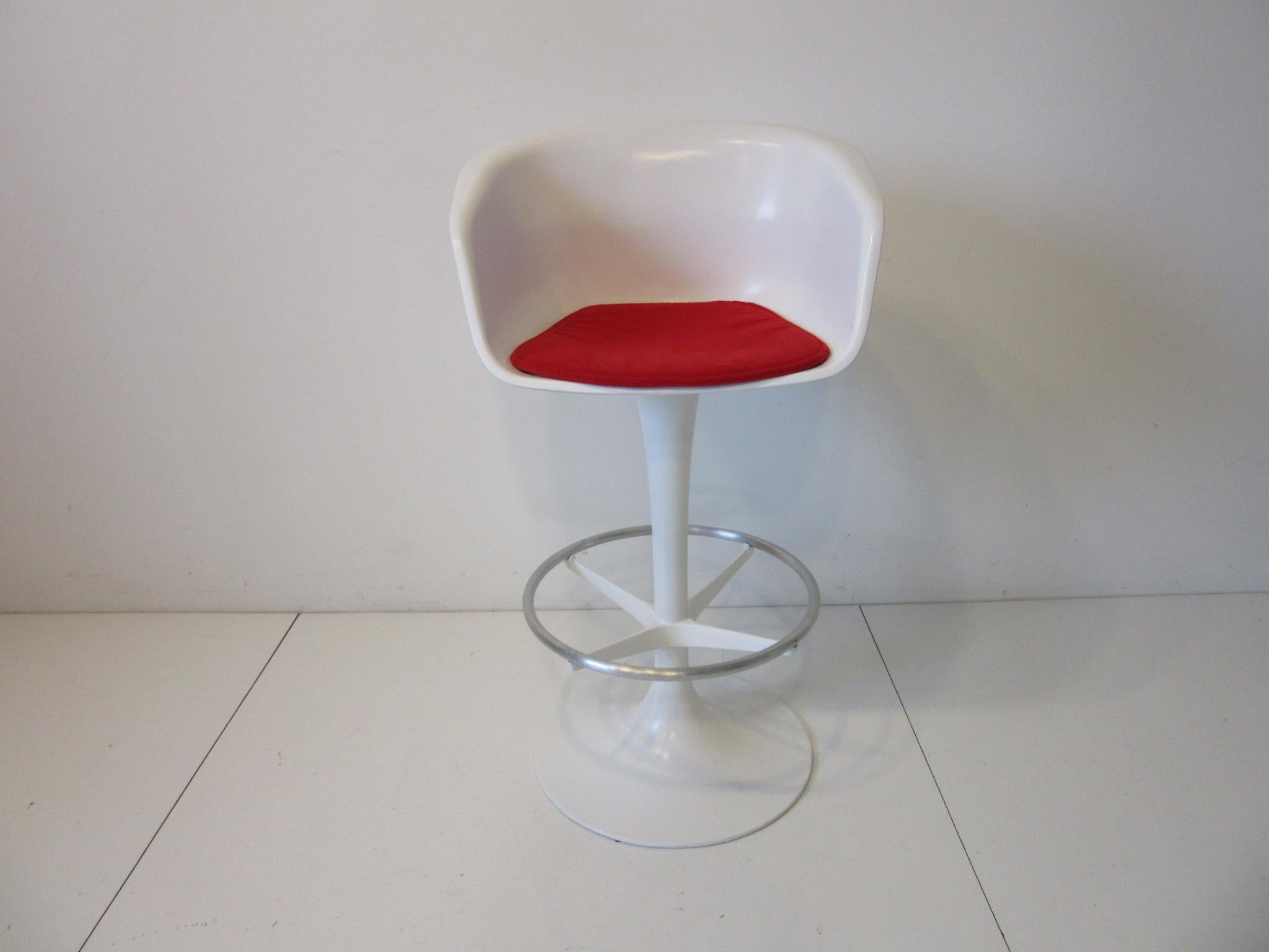 A set of four white swiveling fiberglass bar stools with metal tulip bases, brushed aluminum footrest rings and red fabric seat pads. Designed by Maurice Burke for the Burke Furniture company. The perfect look for that 1970's clean modern design