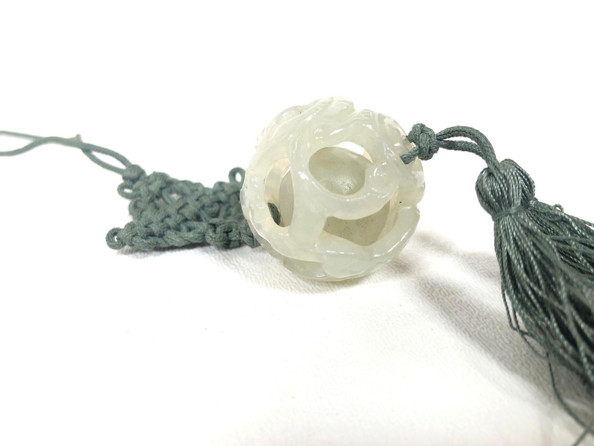 Ce collier vintage en jade trémolite présente une perle de jade ajourée, sculptée à la main, enfermée dans sa cage de jade, suspendue à une corde de soie nouée avec un nœud et une pampille traditionnels chinois. Symbole d'harmonie et de protection,