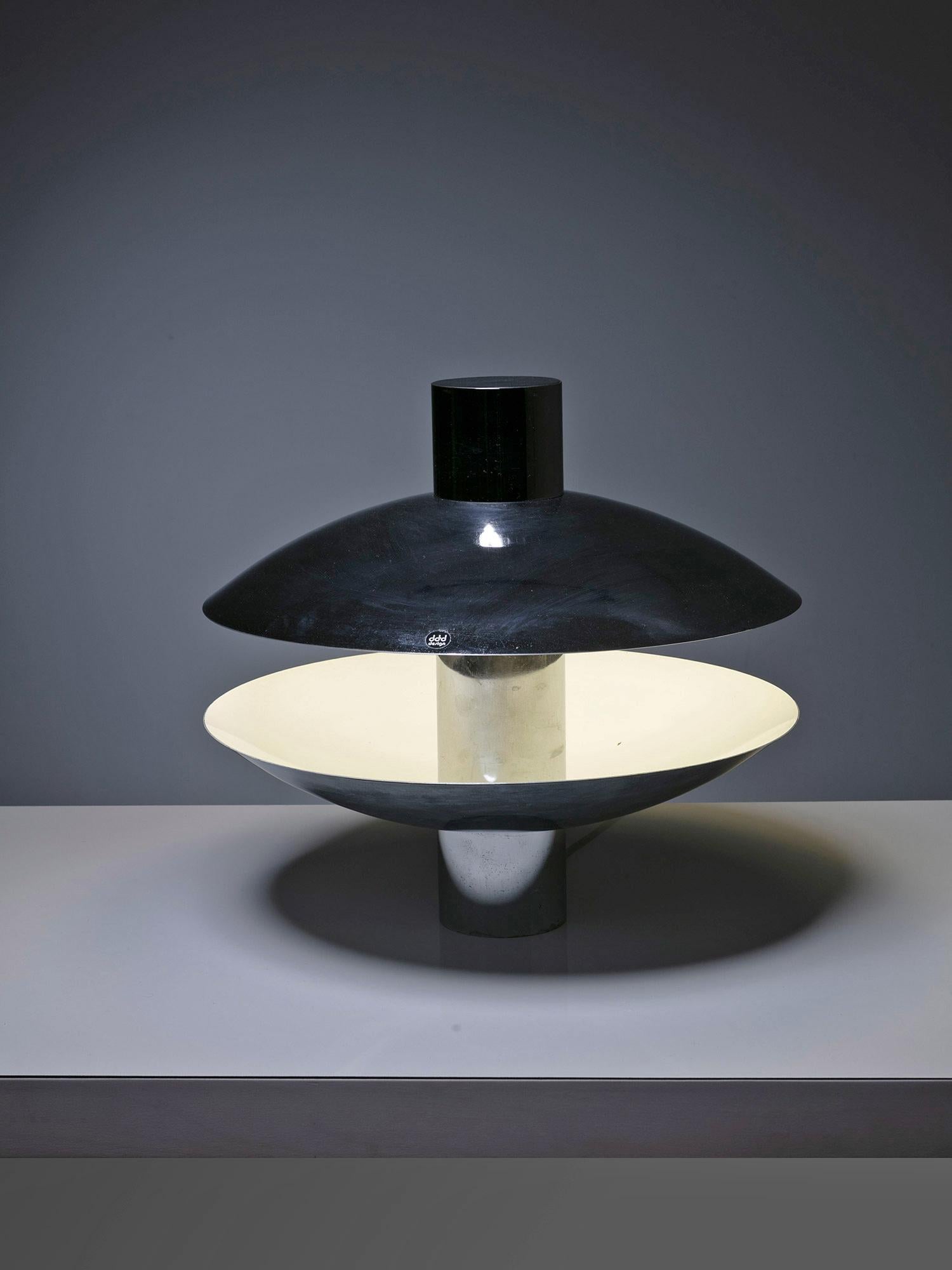 Large chrome table lampmanufactured by DDD Design.
Two symmetrical metal shells hide the light source, providing a space-age atmosphere.
