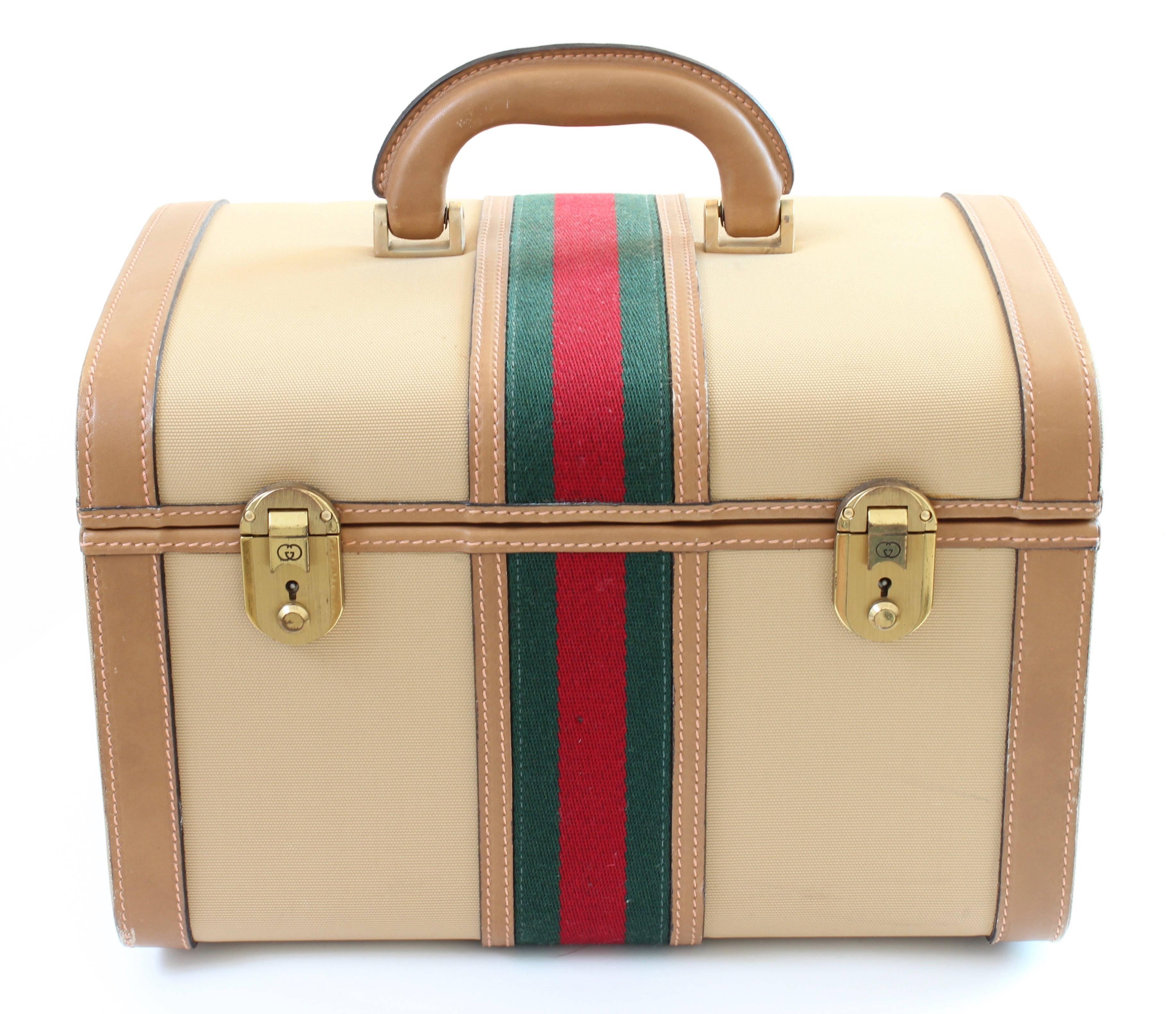 This vintage train case was made by Gucci in the late 1970s.  Made from beige canvas with tan leather trim, it features their signature red and green webbing at the center with gold hardware. The interior has a mirror, is fully-lined and has room
