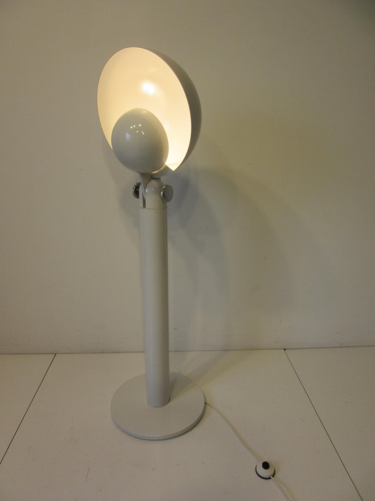 A great Pop Art white metal floor lamp with articulating hemisphere domed shade controlled by two large polished aluminum knobs with a small ball and a wing inside to defuse the light source. The shade can be adjusted down or at many angles for in