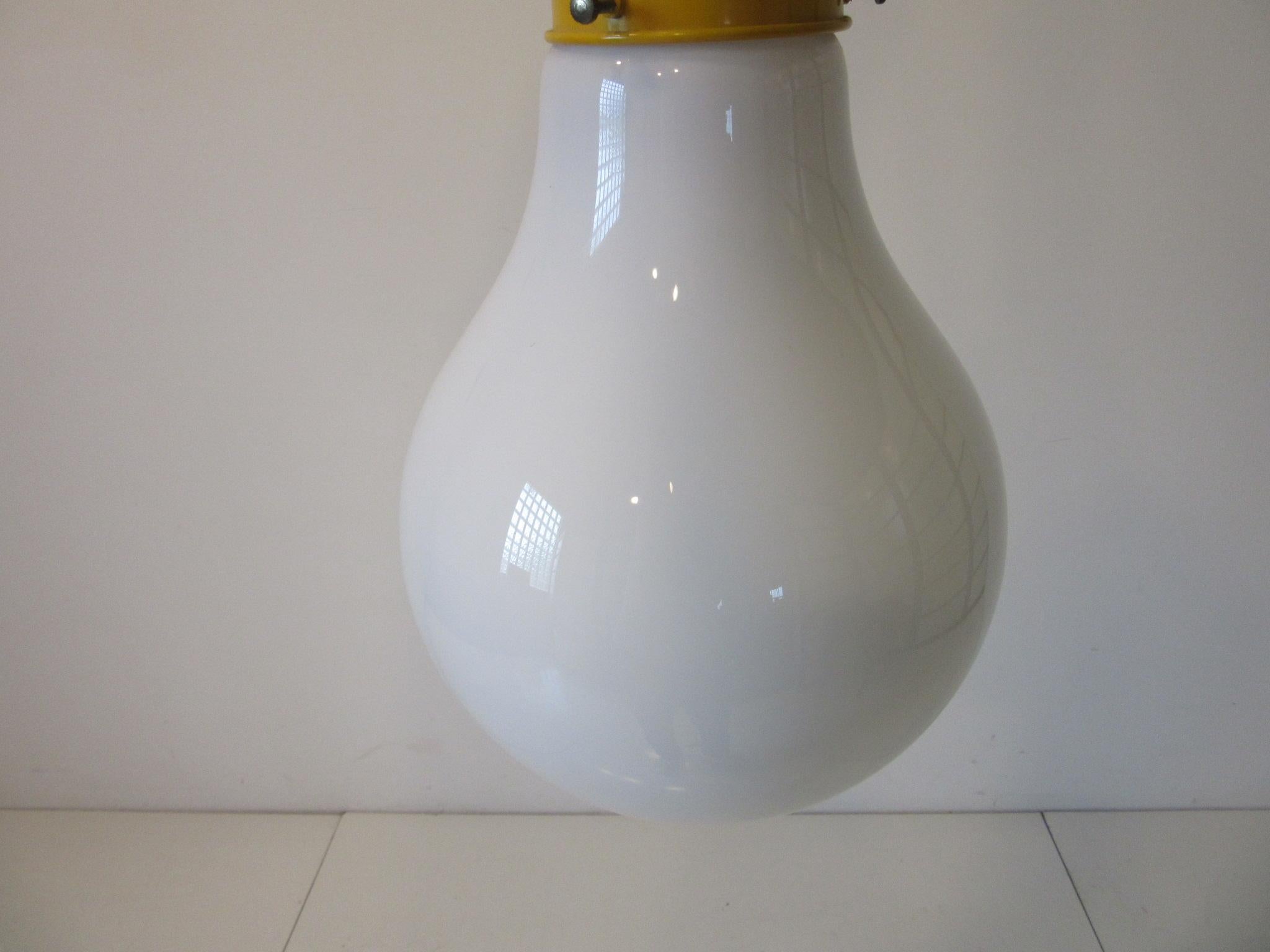 An oversized Pop Art styled hanging light bulb with blown white glass shade and yellow metal cap. Includes the original brass swag hanging chain at 130