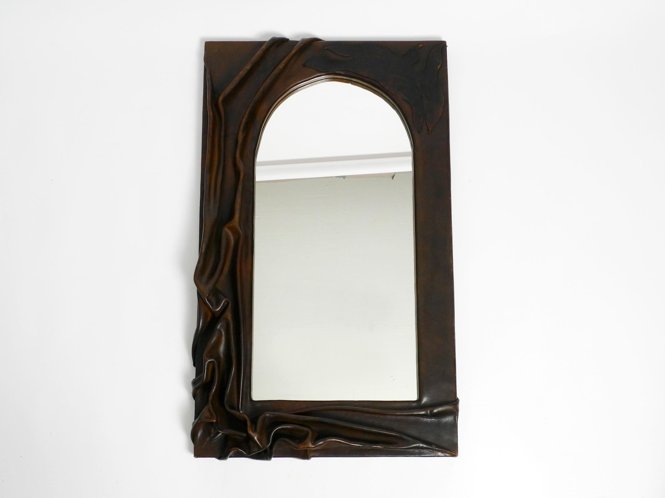 Beautiful rare large wooden wall mirror with artful thick leather cover. Handcrafted in the 1970s. Each of those mirrors is unique.
Very elegant sculptural design made of thick, solid cowhide. Mirror glass is without damages. Not blind.
The leather