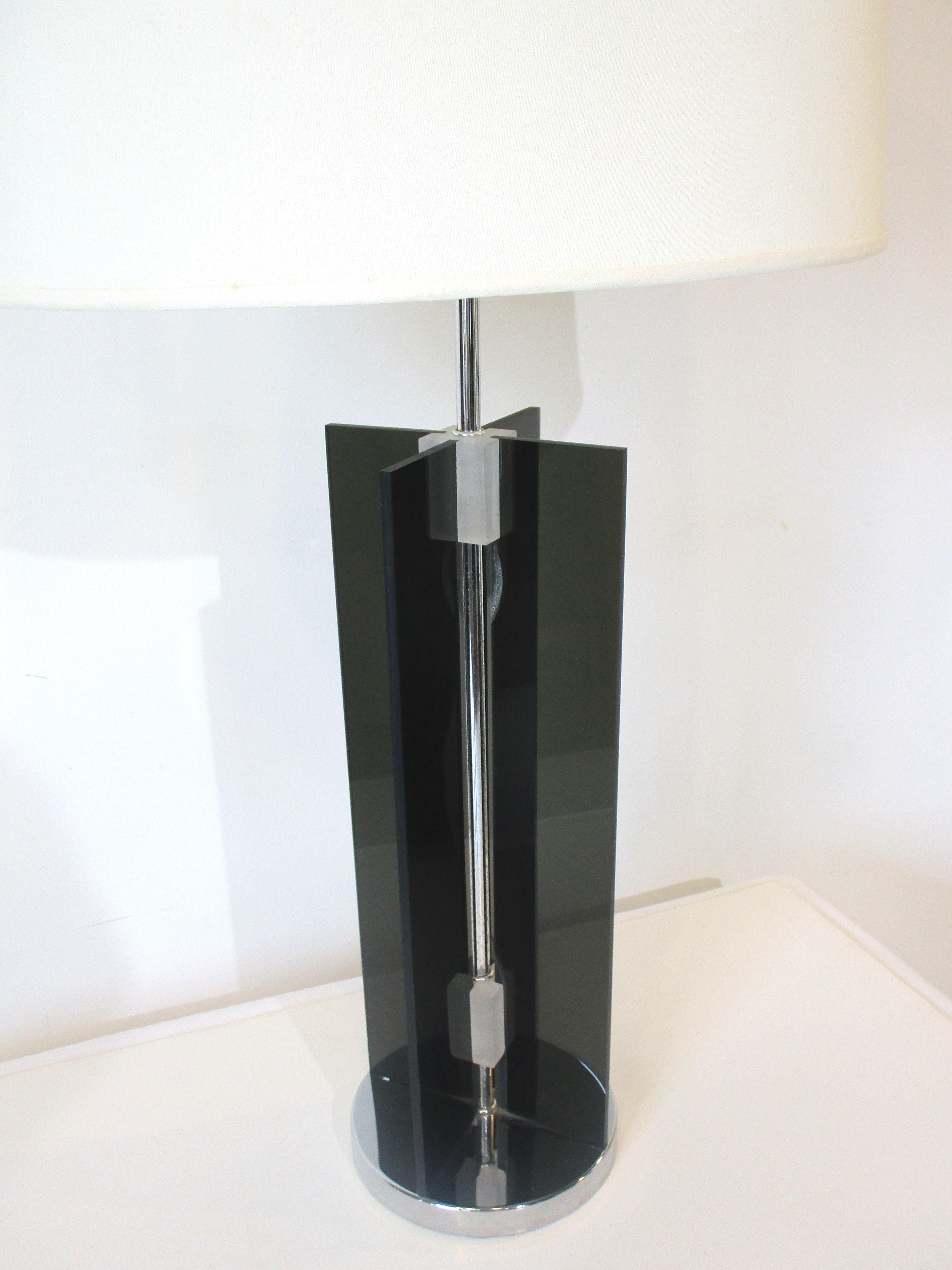 A smoked Lucite table lamp with a X shaped two planed body mounted on a chromed circular base. The body is held together by frosted Lucite rectangle pieces giving the lamp a great look, simple but also well crafted in the manner of Neal Smalls.