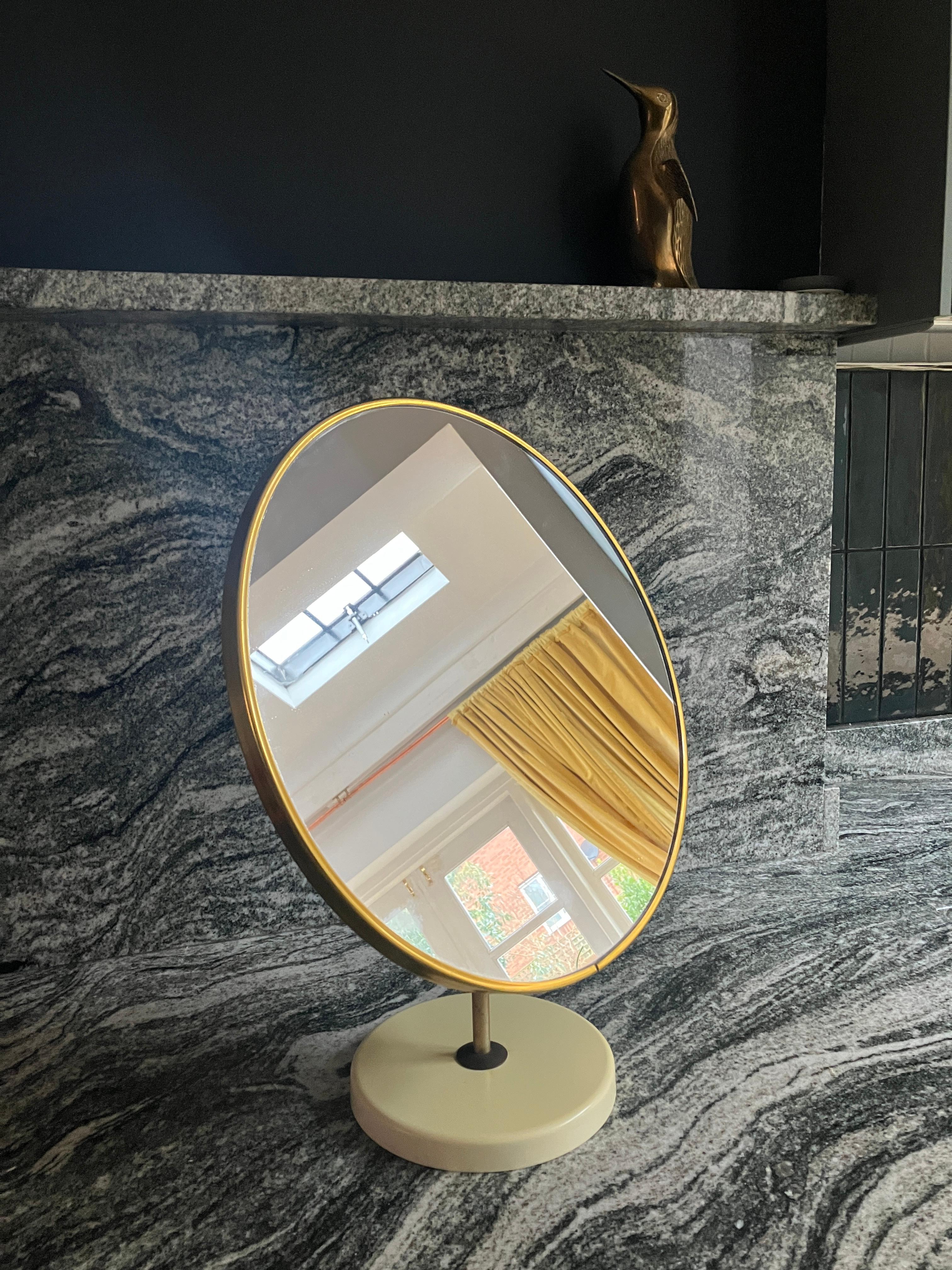 Large mid-century modern round vanity mirror. This 70's vintage table mirror has lovely proportions with a large mirror. The mirror is edged with a brass trim and the metal pole is finished in brass, too. The cream plastic stand makes the mirror