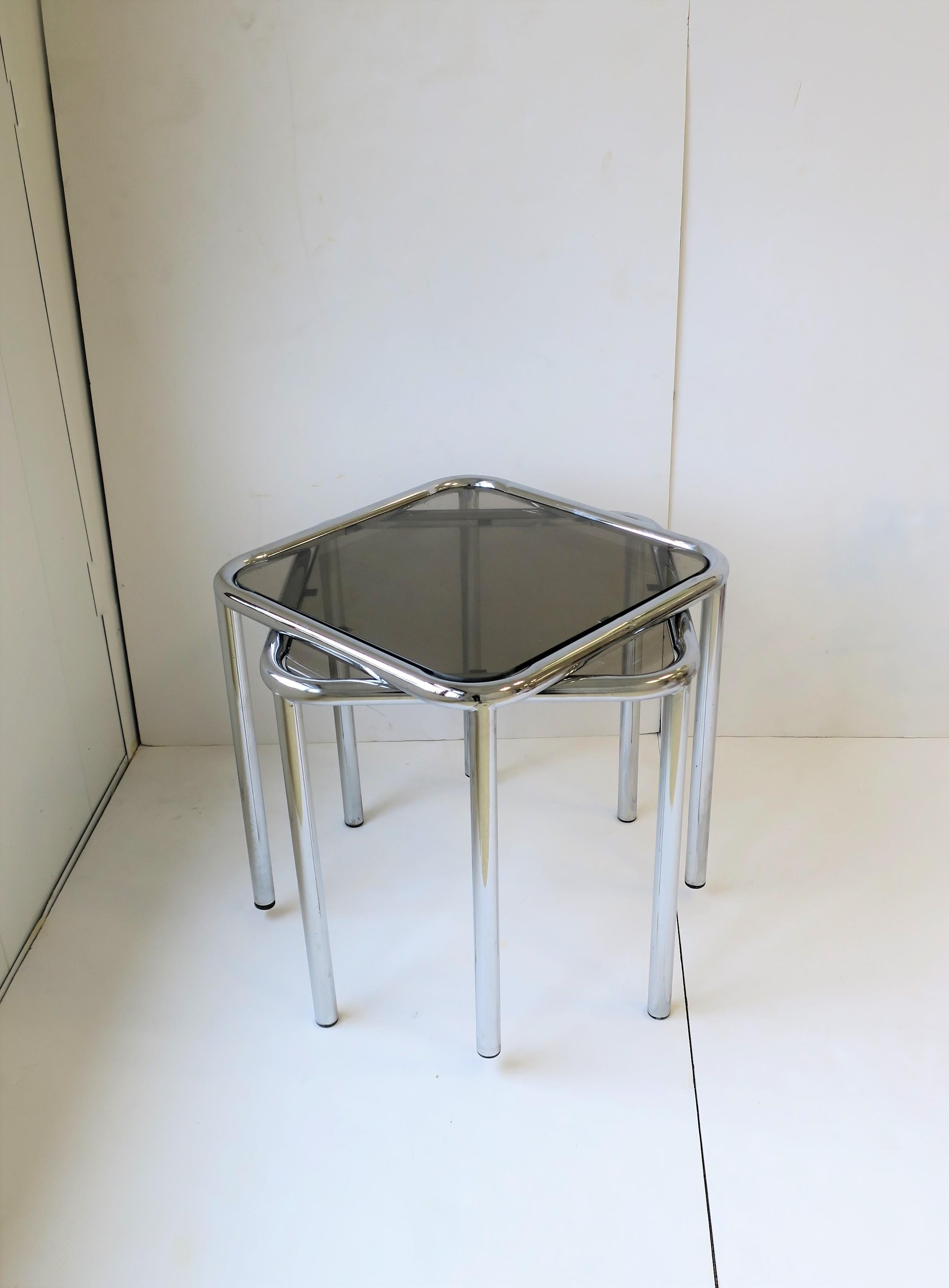 A substantial set/pair of end, side, and stacking tables, circa 1970s Modern or Postmodern period. Base frames are a tubular chrome and tops are a smoked glass, both finished with rounded corners. Glass sits 'in-set' into table frame/base. Tables