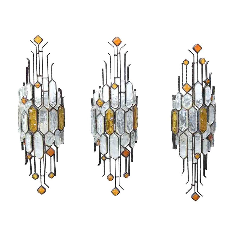 These wall lights are a stunning pair of artistic sconces. They feature a brown enamelled wrought iron structure with rock-shaped clear and amber hammered glass. Designed by Longobard in the 1970s, these Italian wall lights have a touch of Art
